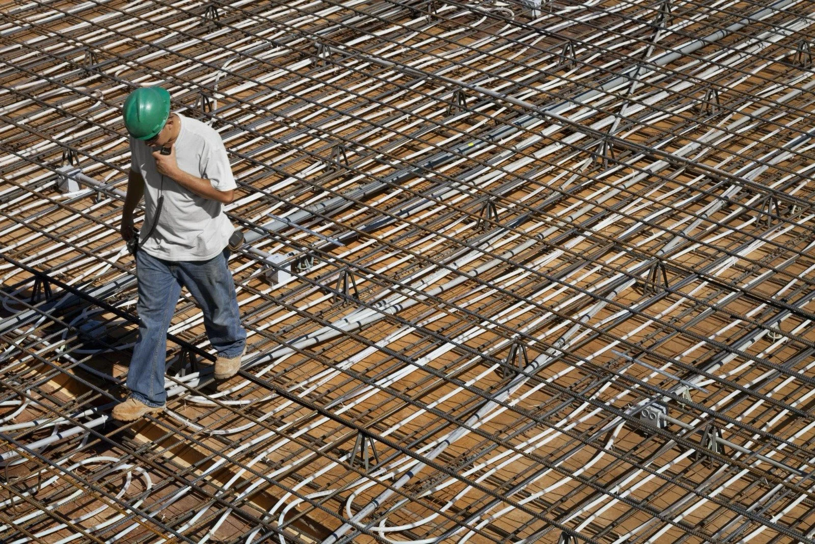 Construction worker walking on rebar and electrical conduit at a building site