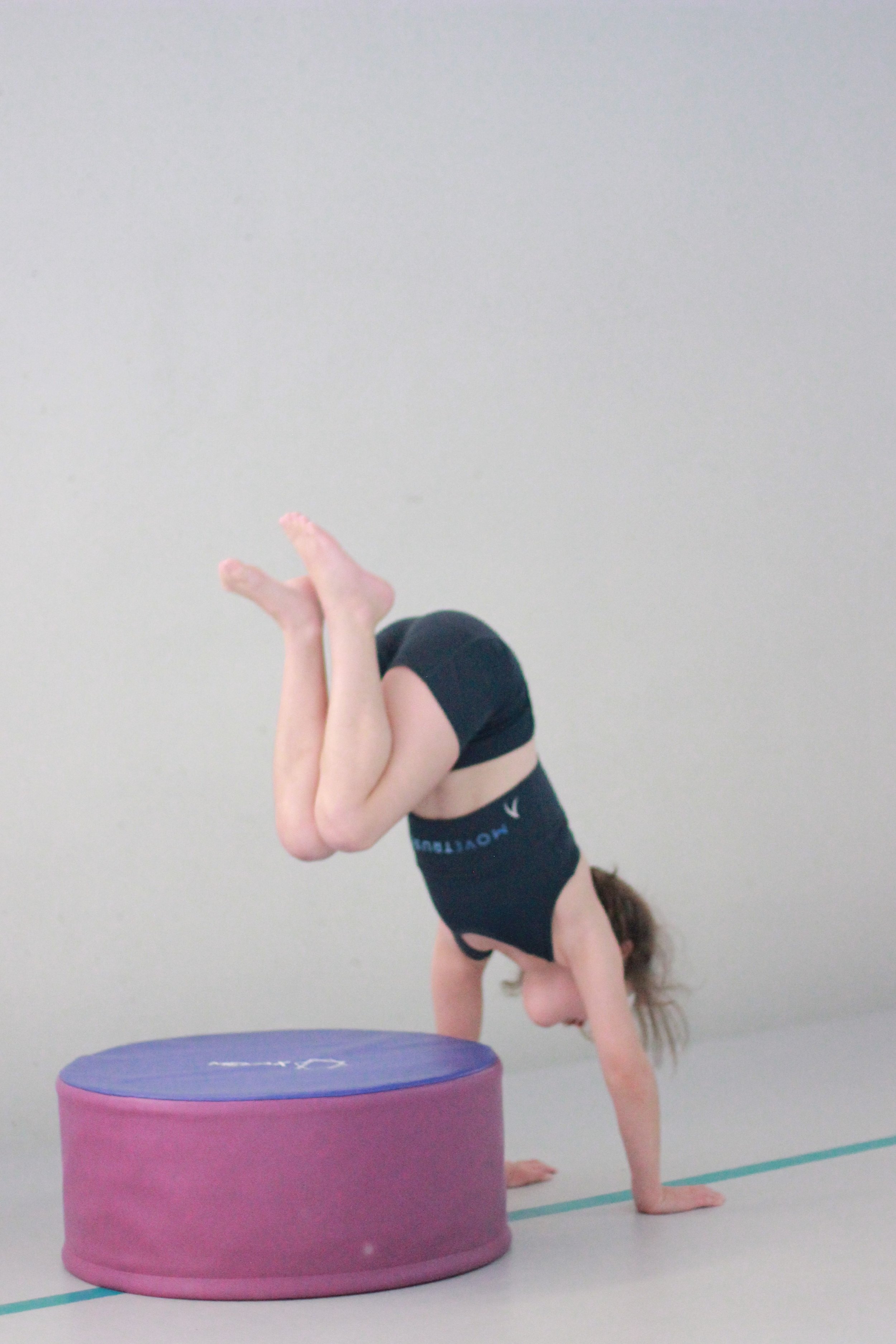 VHGC gymnast doing a donkey kick on an air track next to a purple foam block