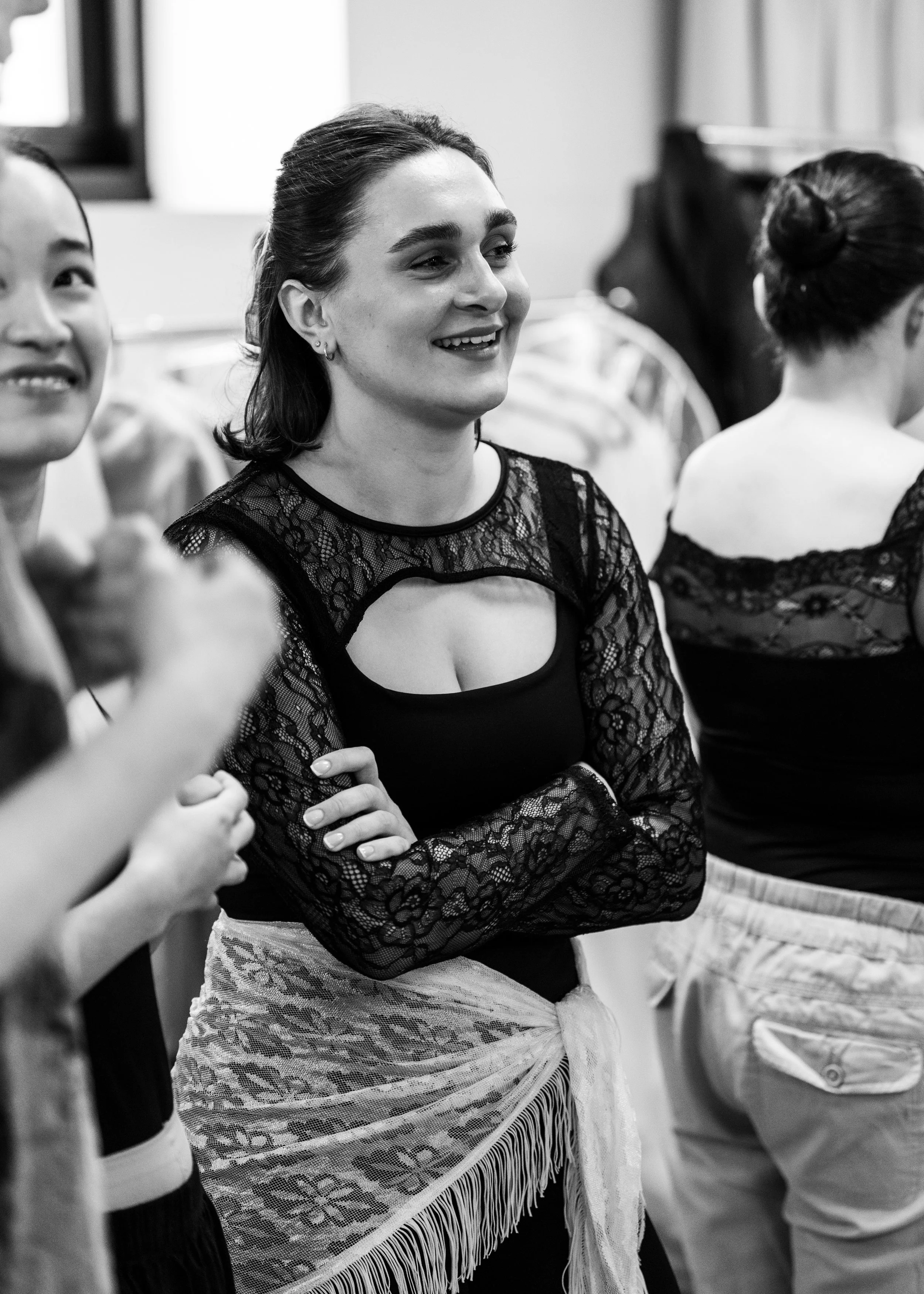 Black and white photo of women standing together, some with arms crossed, smiling and looking at the other dancers back stage at the Shirley Burke Theatre