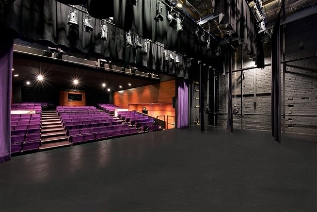 Shirley Burke Theatre empty, in coloured photo from side stage curtains, hanging stage lights, and an empty auditorium with rows of seats, before the AABC Competition begins.