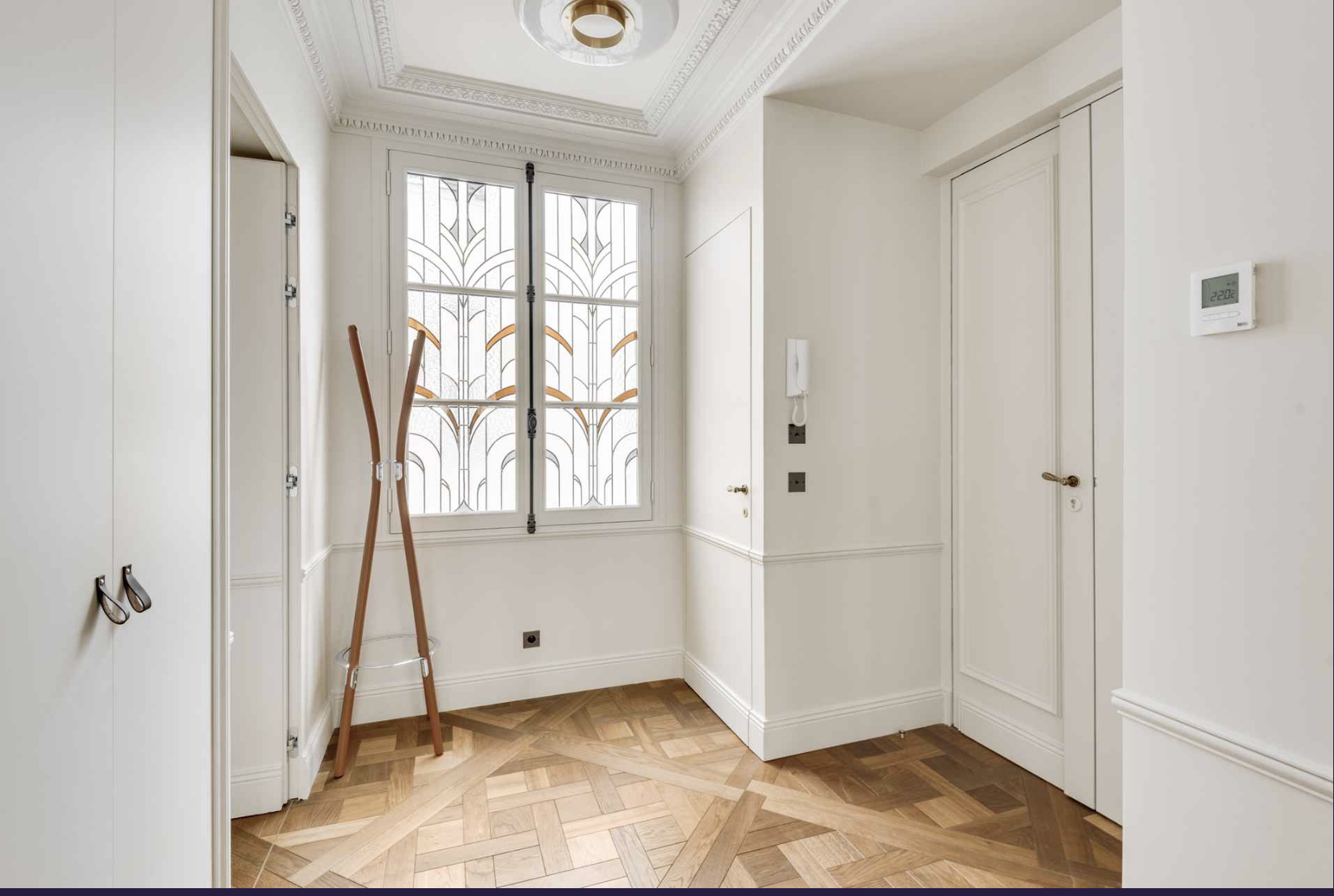 Empty room with wooden flooring, white walls, a window with decorative glass, a white closet, a wall-mounted thermostat, and a coat rack.