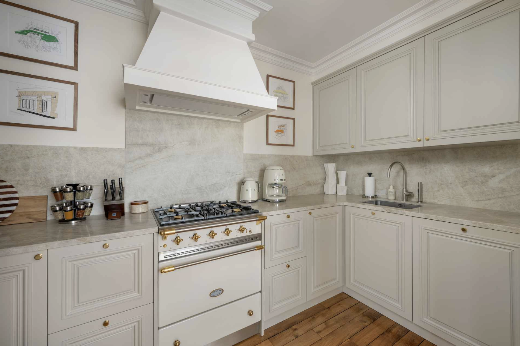 A white kitchen with cream-colored cabinets, a beige countertop, a gas stove with a vent hood, and decorative framed artwork on the wall.