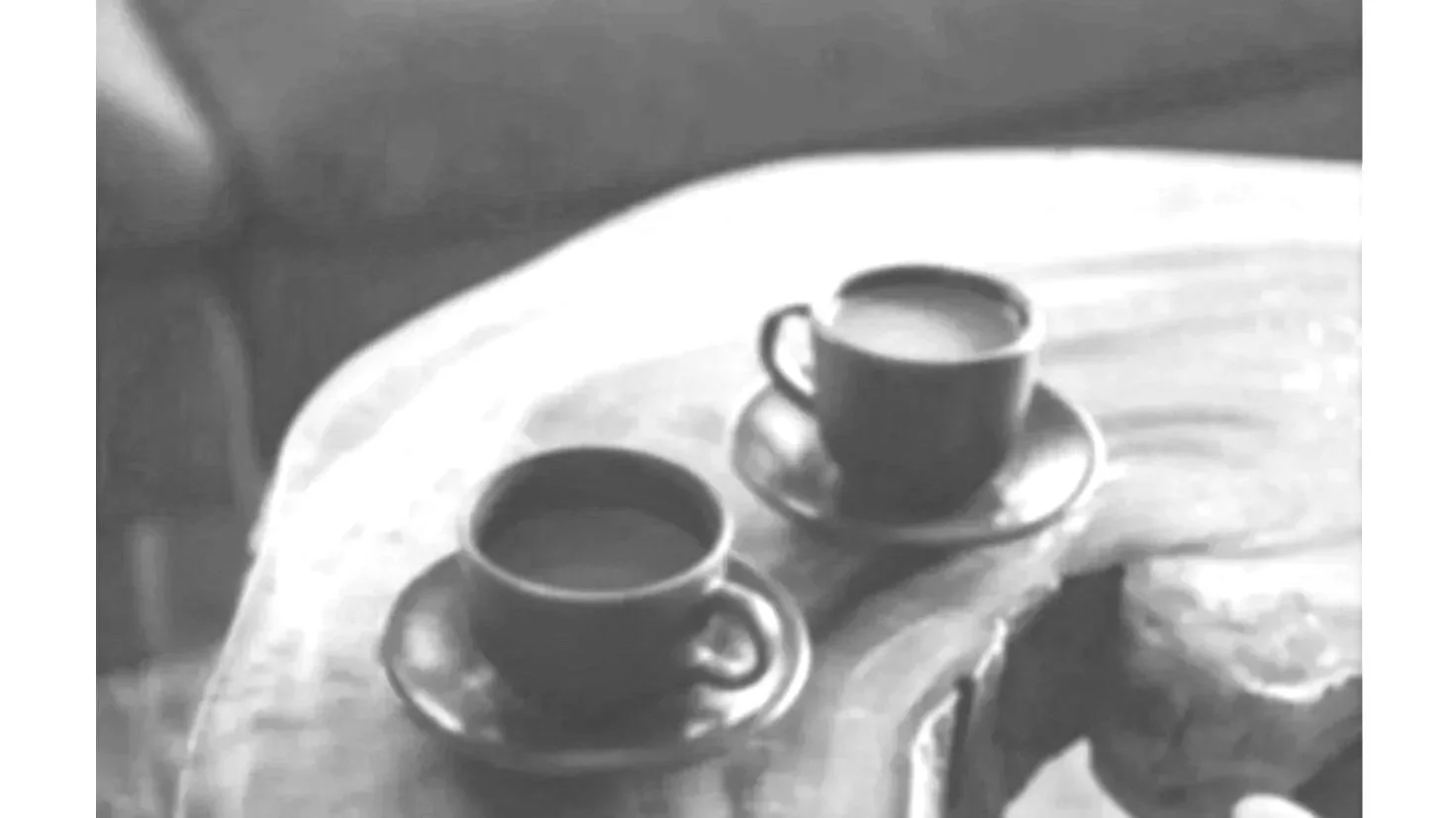 Two black coffee cups on matching saucers placed on a round wooden table.