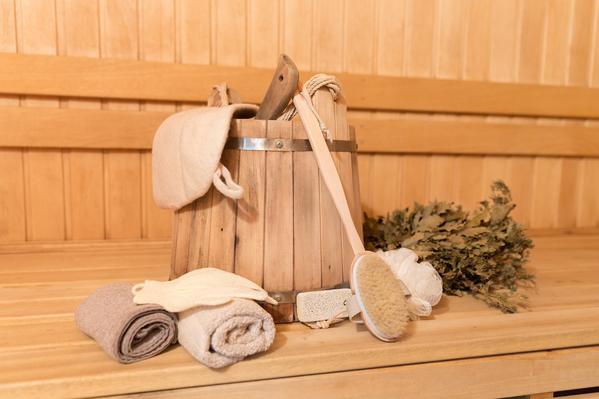 Sauna-Zubehör mit Sauna-Eimer, Harke, Rollen, Tüchern, und Kräutern auf Holzbank