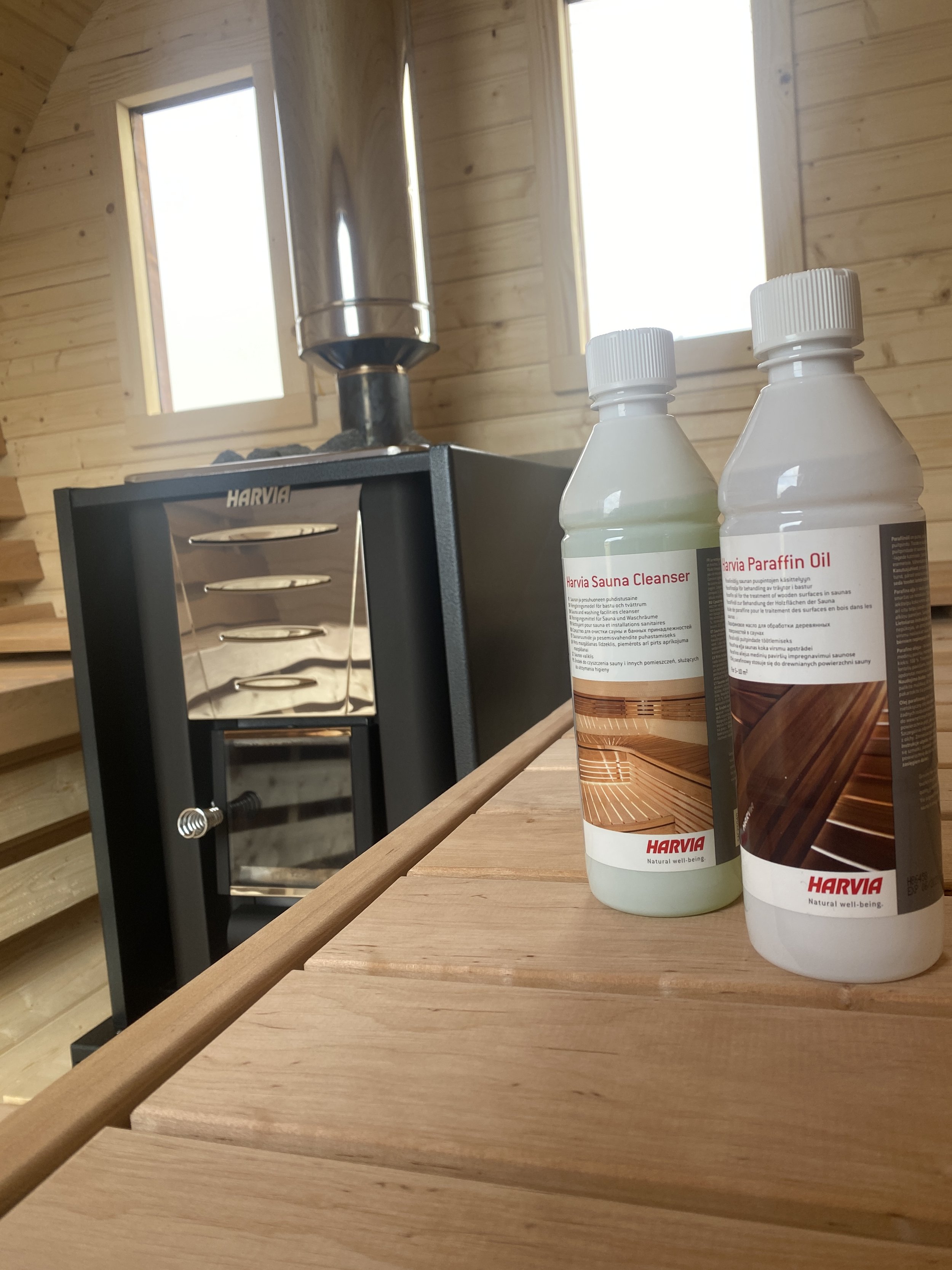 Zwei Flaschen mit Harvia Sauna Pflegeprodukten auf einem Holztisch in einer Sauna mit Holzwänden und großen Fenstern