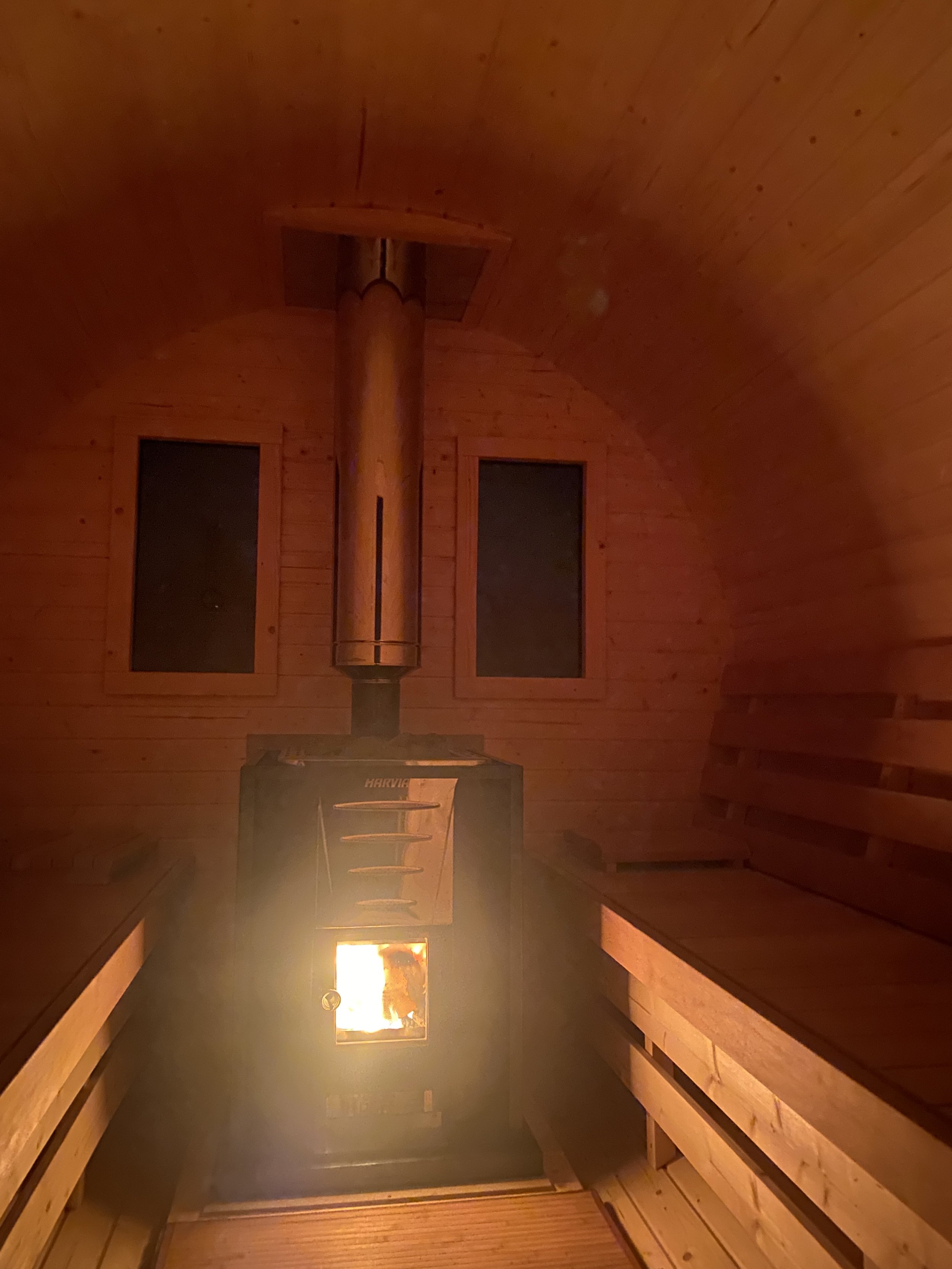 Innenraum einer Saunakabine mit Holzverkleidung und einem Ofen, in dem Feuer brennt.