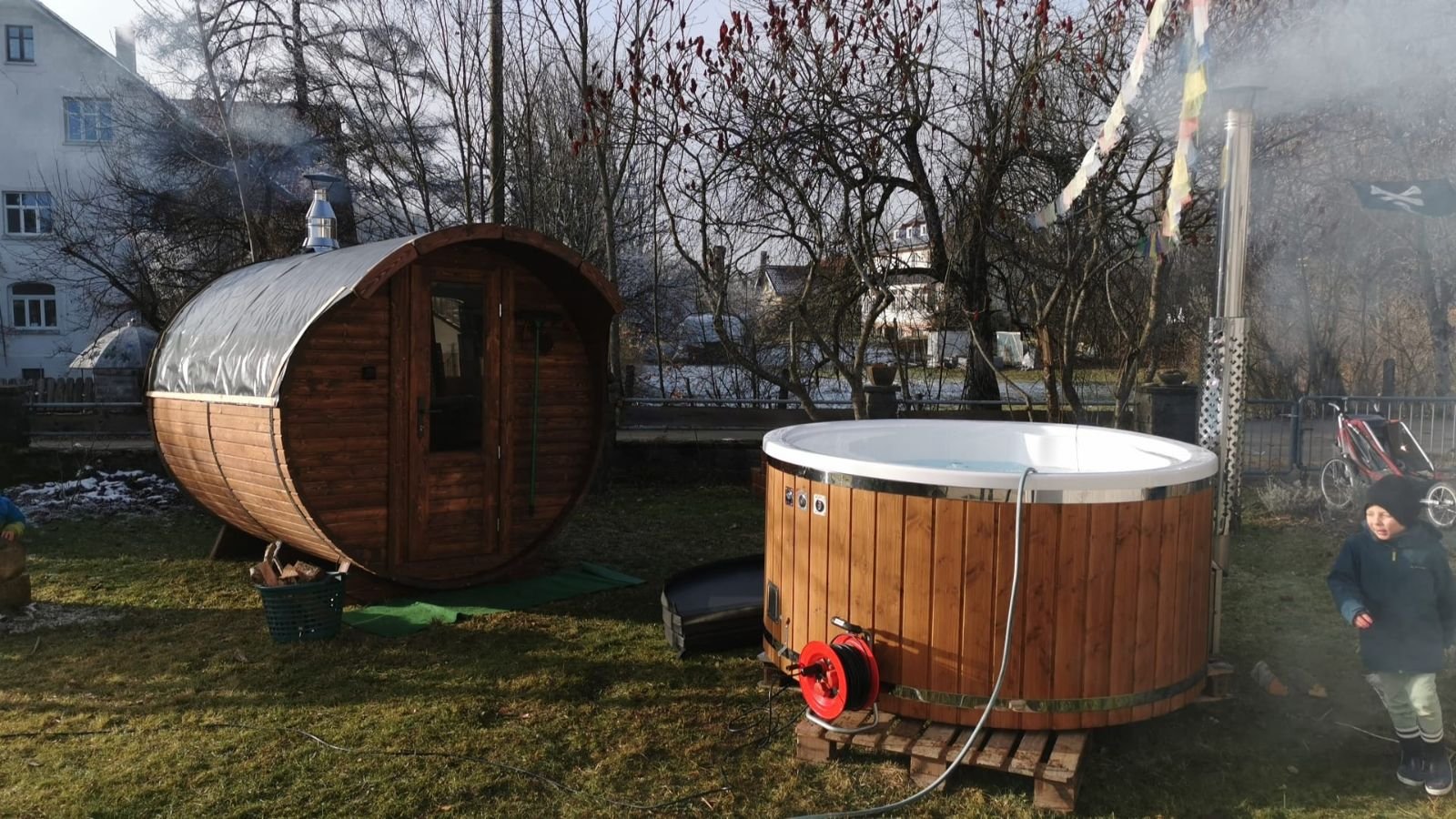 Garten mit Sauna, Hot Tub und Kind, umgeben von Bäumen und Häusern im Hintergrund.