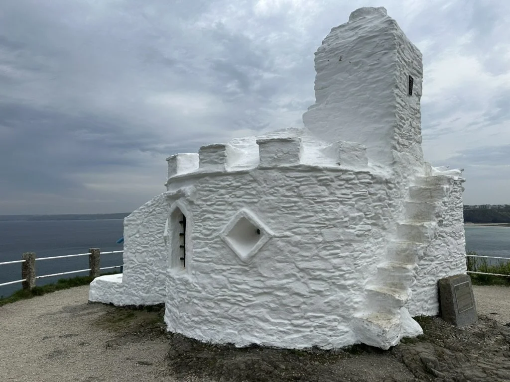 White castle-like structure on a cliff overlooking the ocean under cloudy sky.