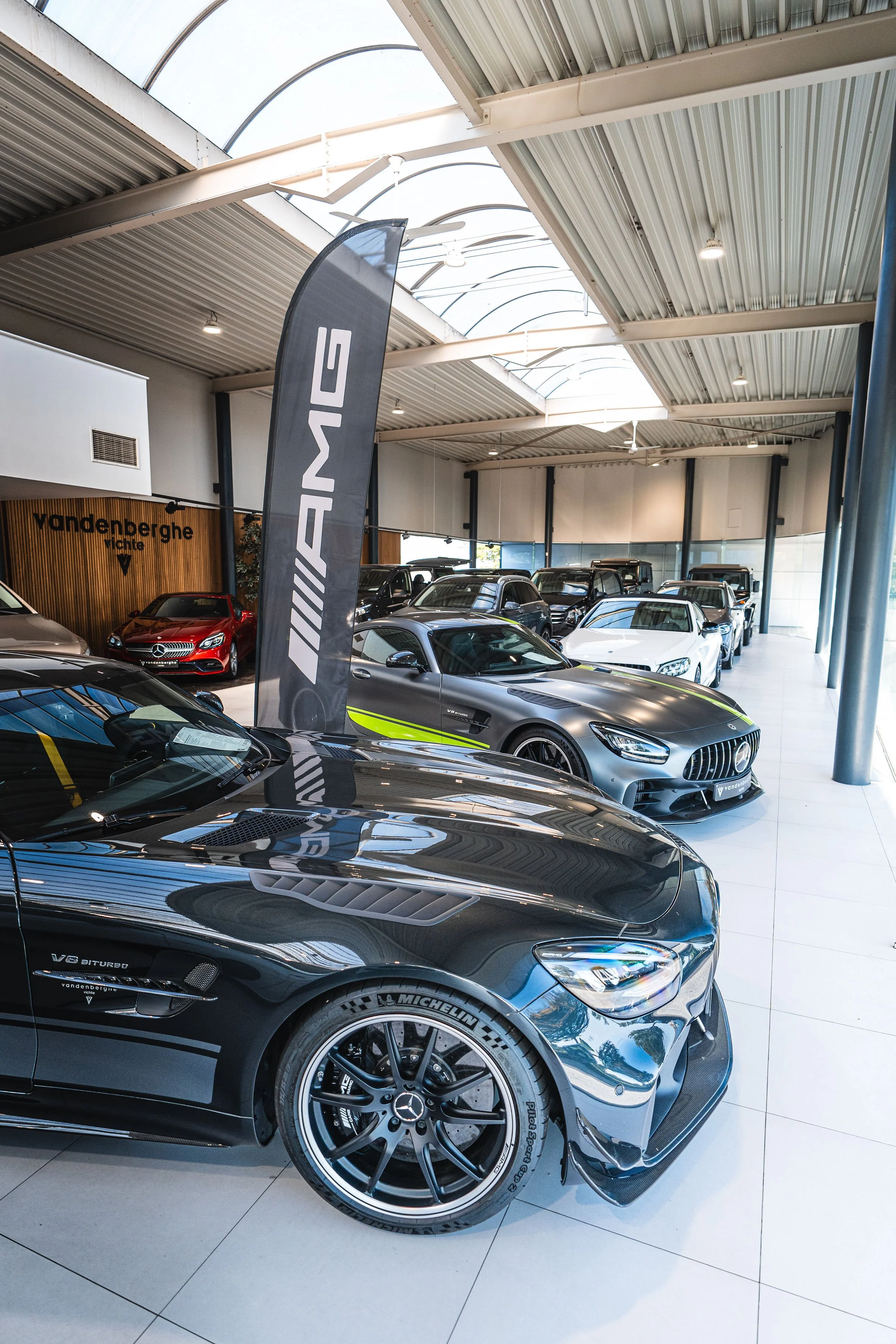 Een grijze Mercedes-Benz auto in een showroom, met een plant op de achtergrond en andere auto's ernaast.