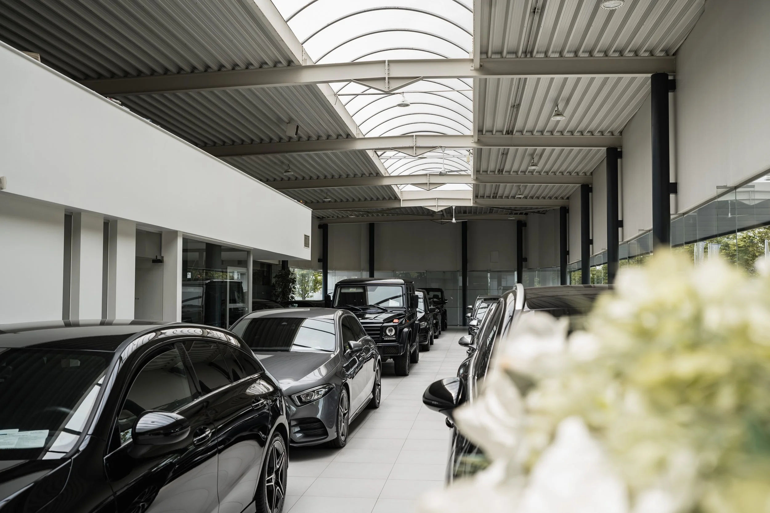 Luxe autodealer met rijen glanzende zwarte en grijze auto's, en bloemen op de voorgrond.