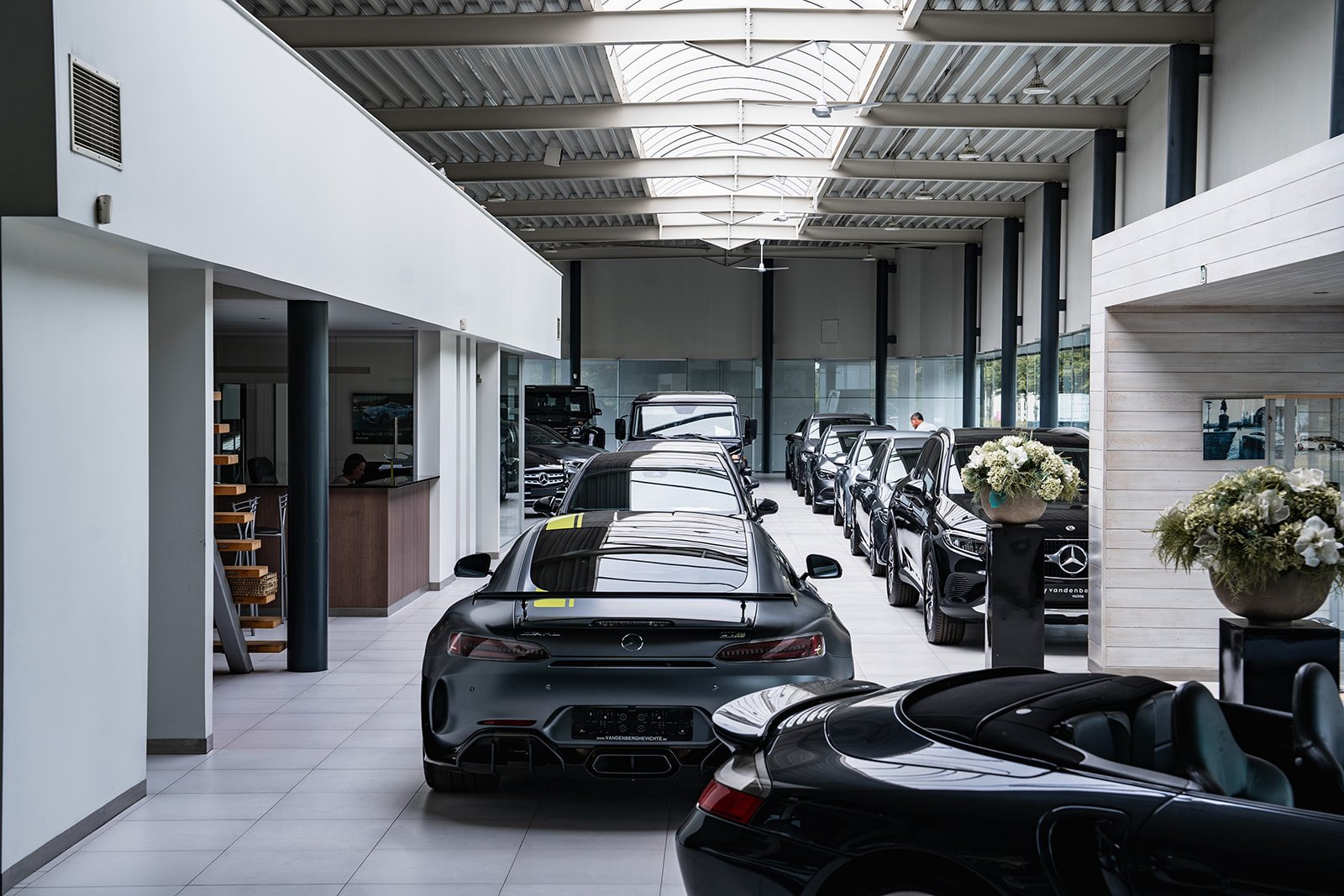 Een grijze Mercedes-Benz auto in een showroom, met een plant op de achtergrond en andere auto's ernaast.