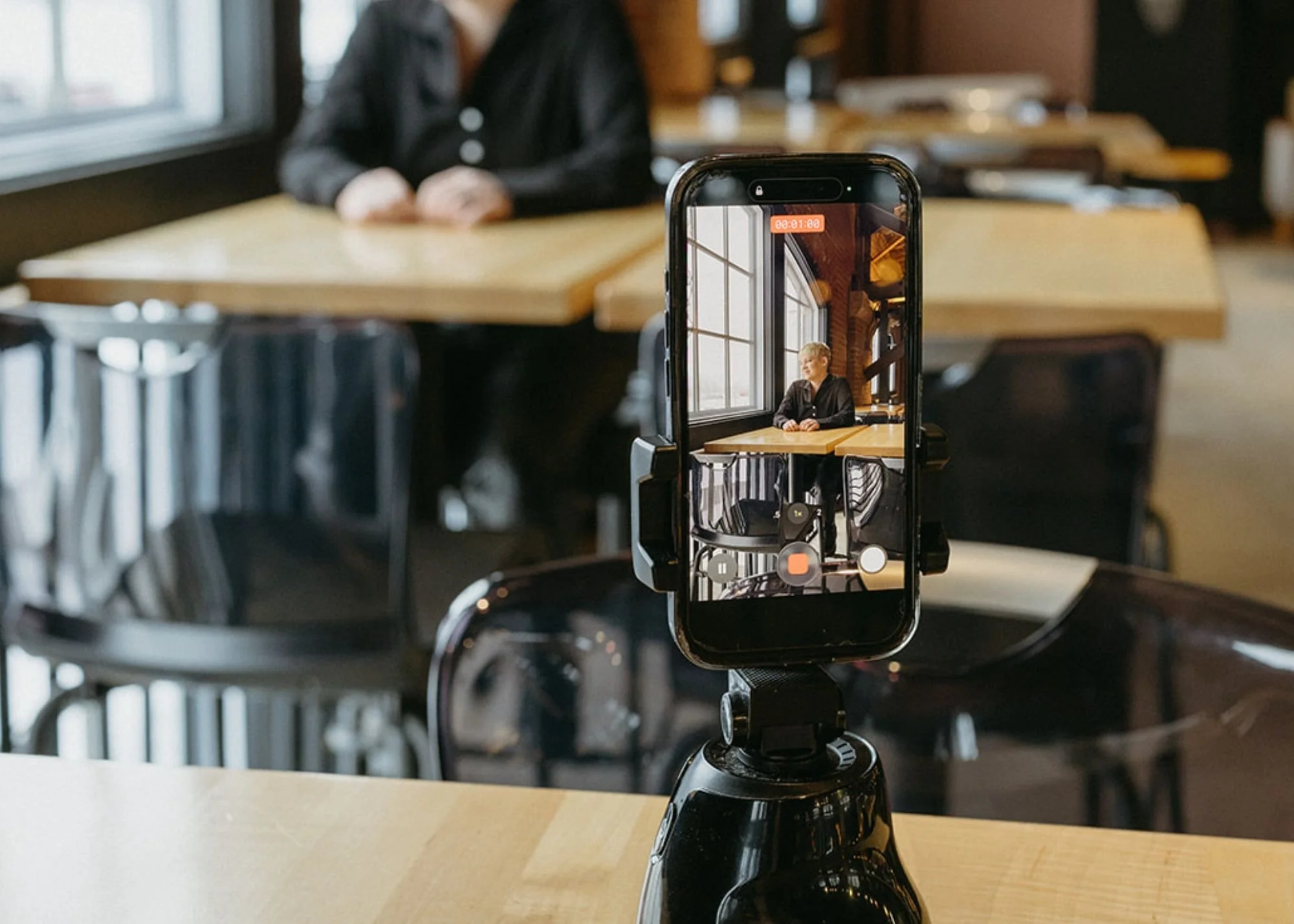 An iphone is positioned on a black holder pointed towards an SEO marketing consultant sitting in the distance
