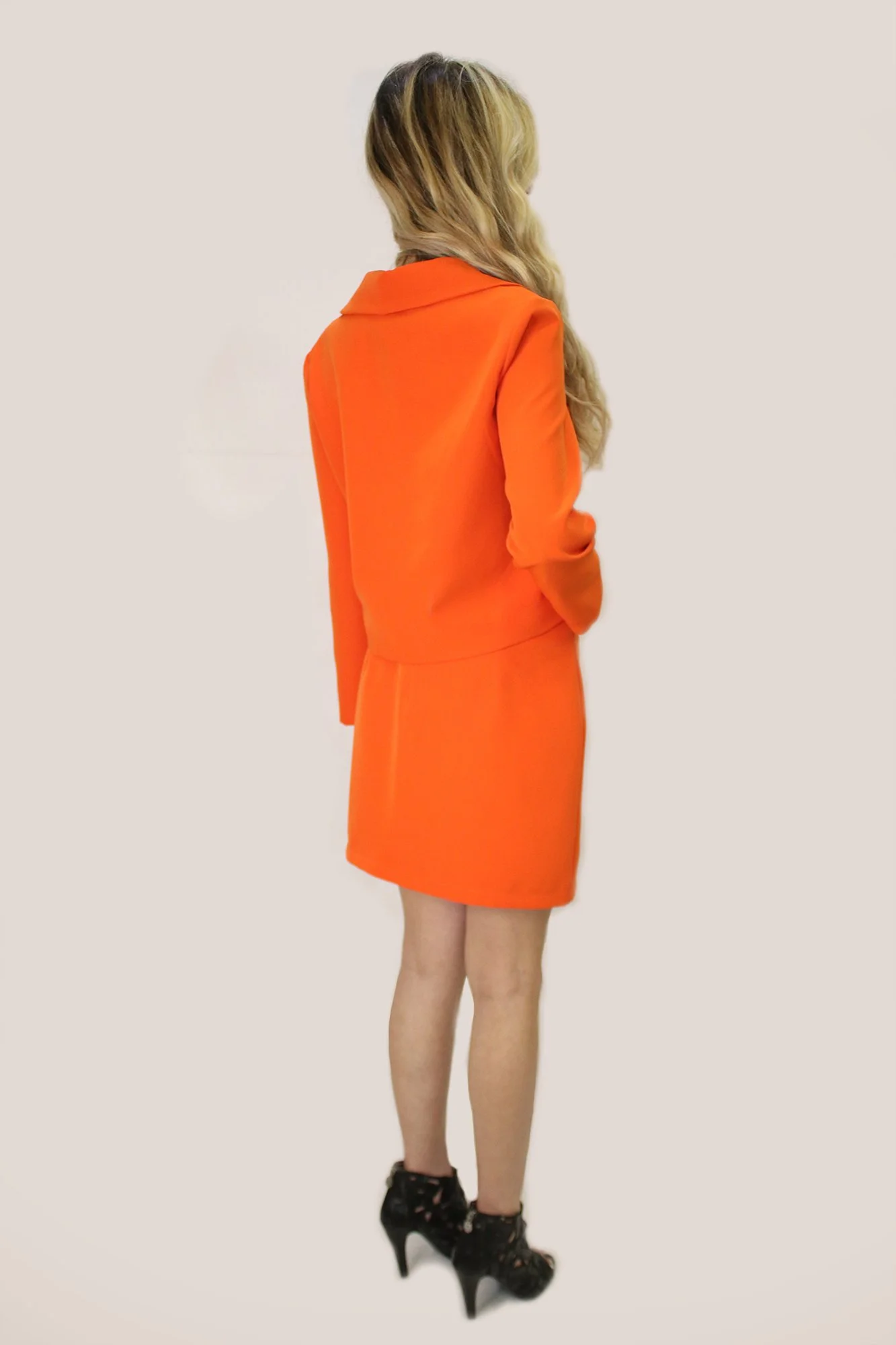 Back view of a woman in an orange blazer and skirt, wearing black high heels with lace.