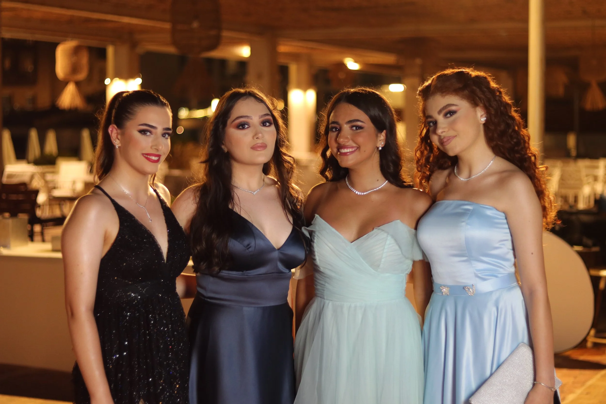 Four young women in formal dresses standing together at an evening event.