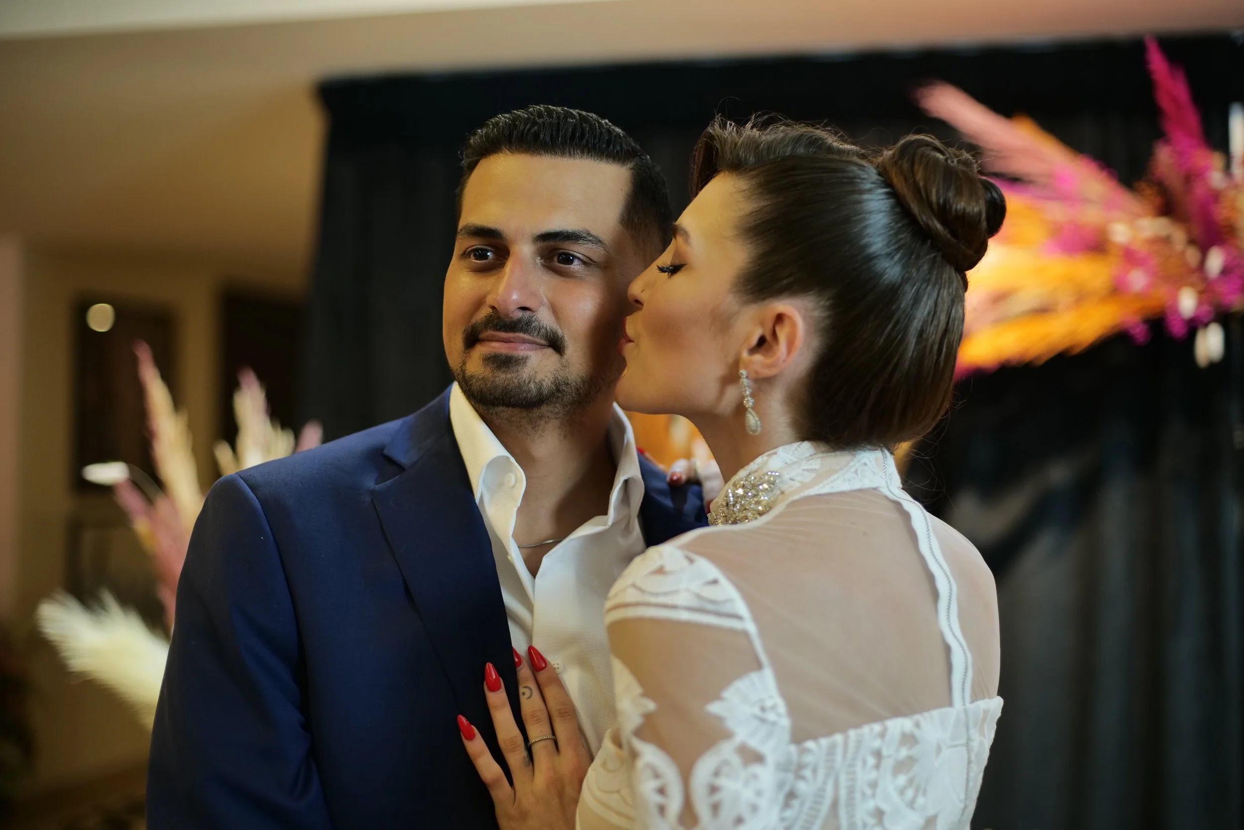 A woman in a wedding dress kissing a man in a suit on the cheek at a wedding reception.
