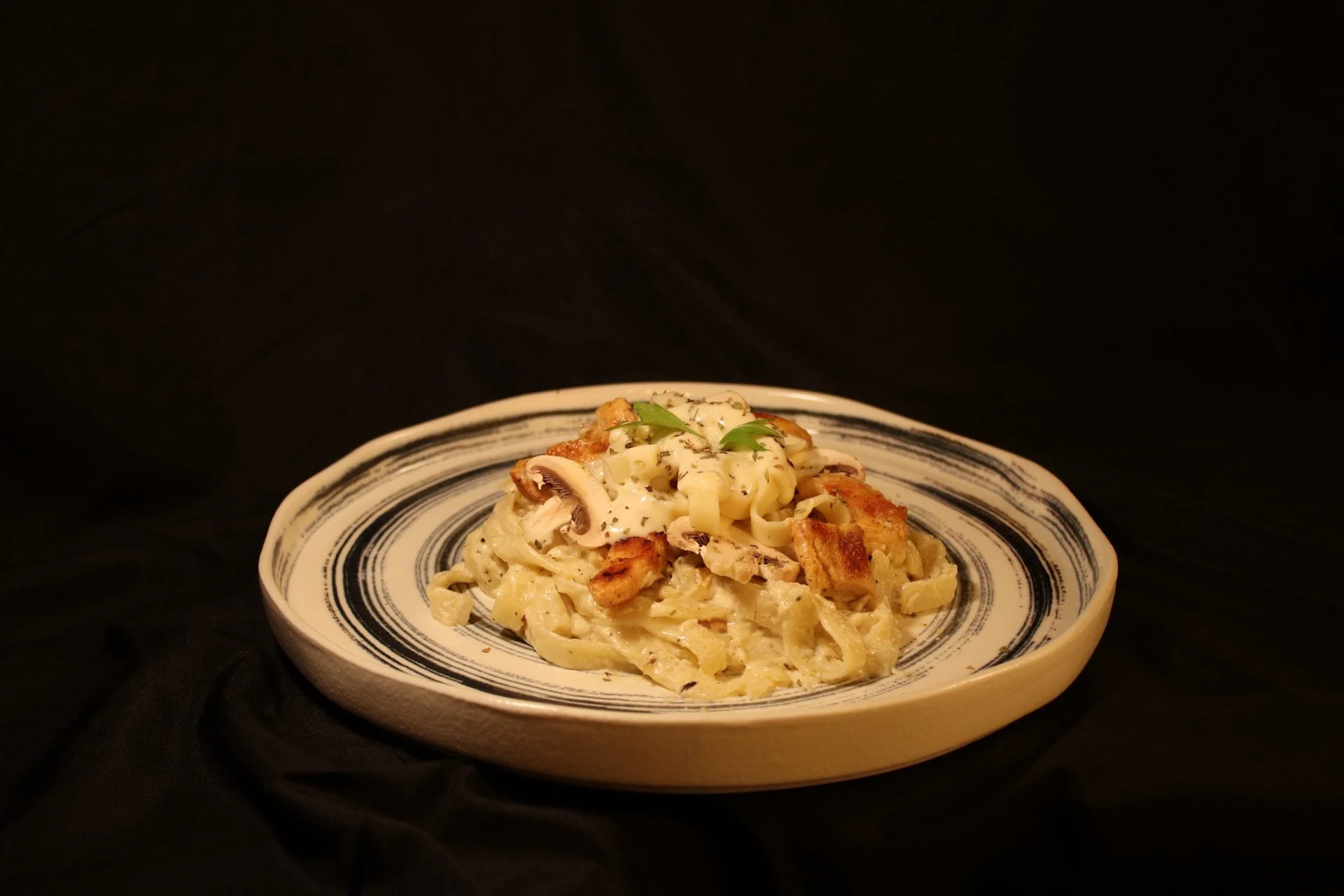Plate of creamy Alfredo pasta with chicken and mushrooms garnished with herbs against a black background.