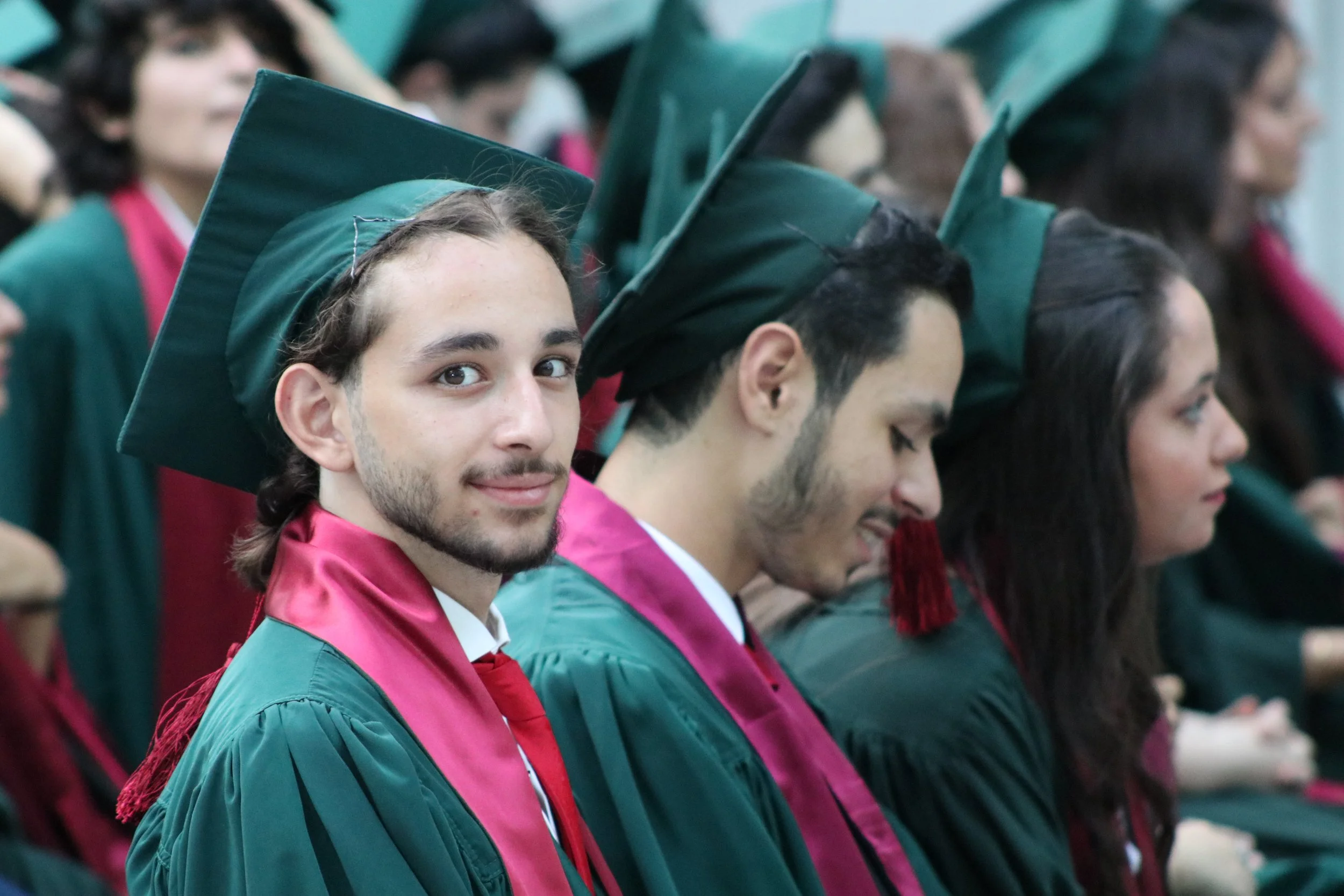 Graduates in green caps and gowns sitting in rows during a graduation ceremony.