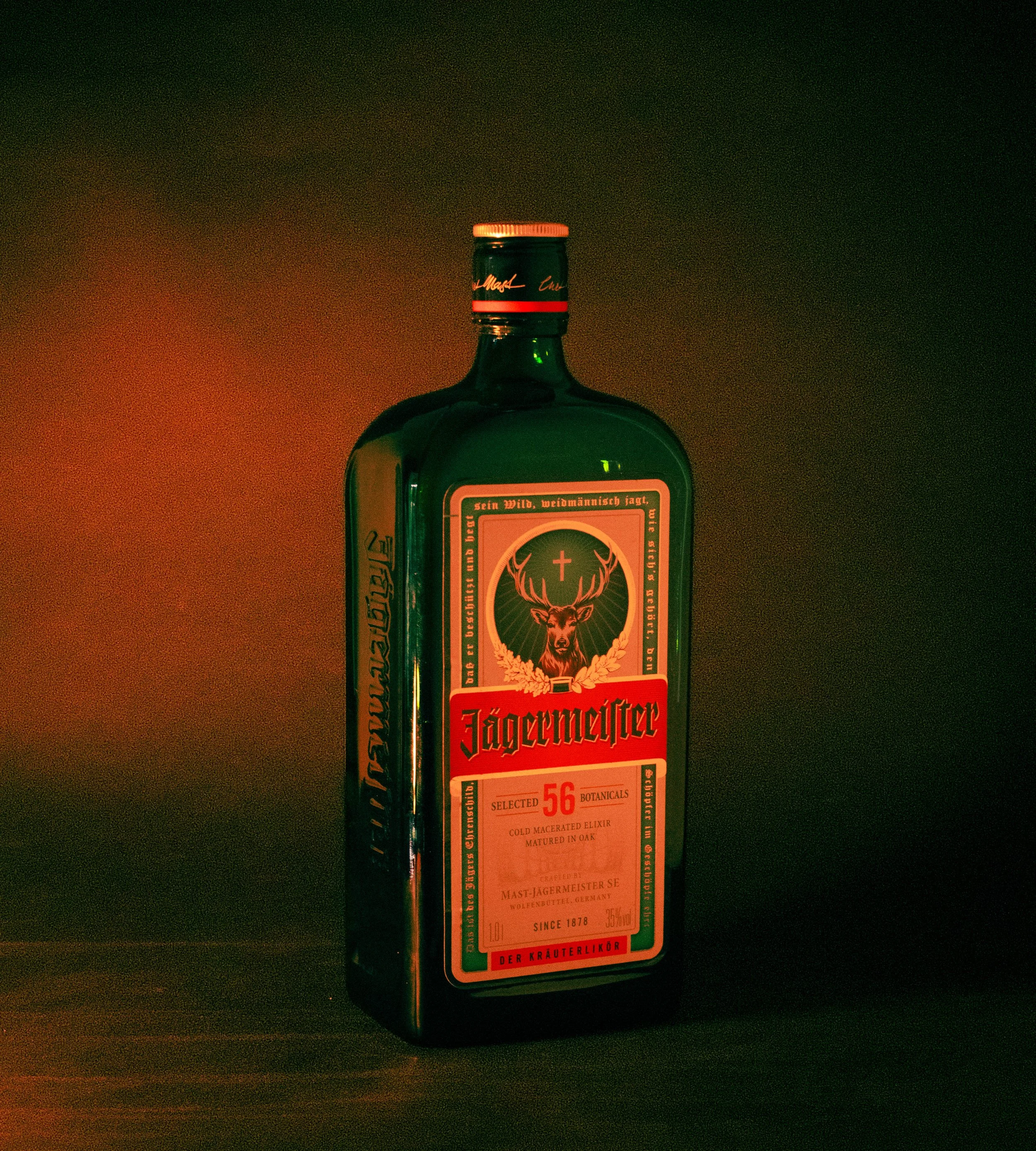 A green bottle of Jägermeister herbal liqueur on a dark surface with a plain dark background.
