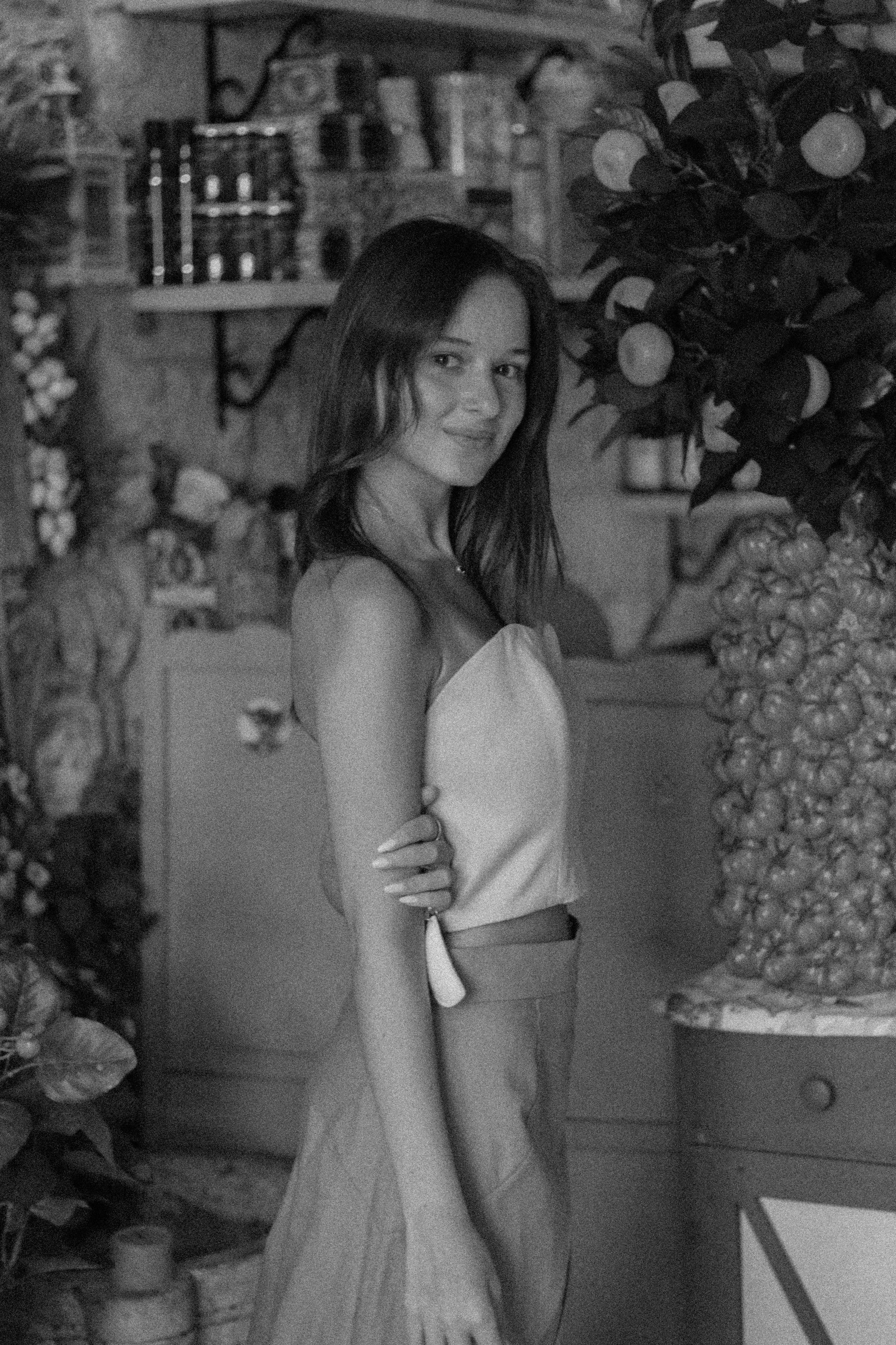 A young woman standing next to a large arrangement of lemons and oranges in what appears to be a shop or market.