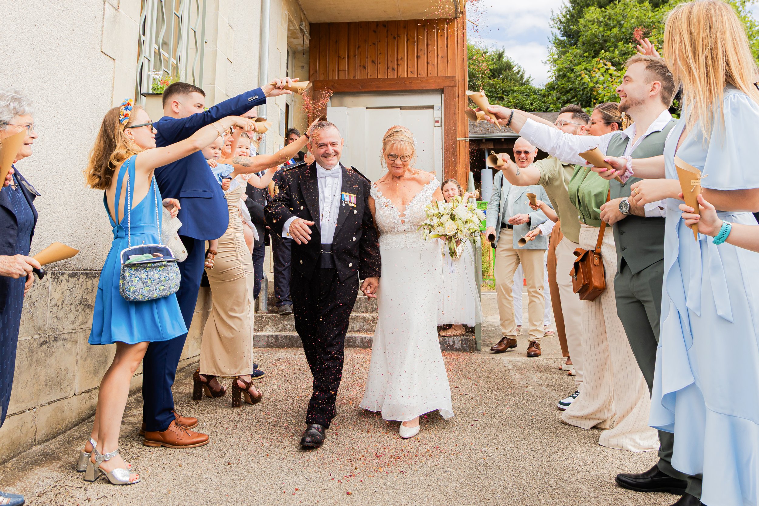 Un groupe de personnes célébrant un mariage en extérieur, lançant des confettis sur un couple de mariés.