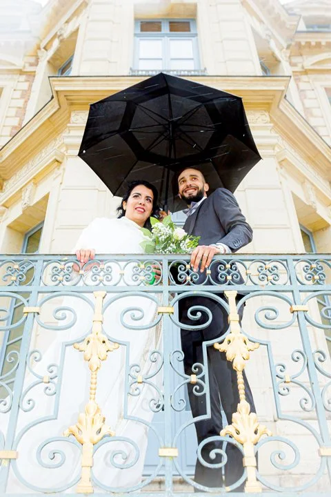 Couple de mariés sous un parapluie devant un château à Tours, ambiance élégante et romantique malgré la pluie
