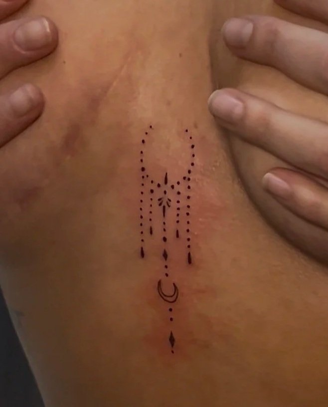 Close-up of a person with a dotted tattoo on their side, being touched by hands with rings.