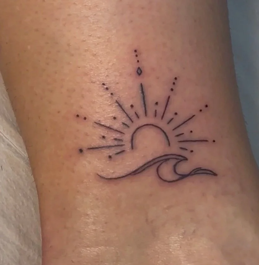 Tattoo of a sunrise over a wave on a person's thigh.