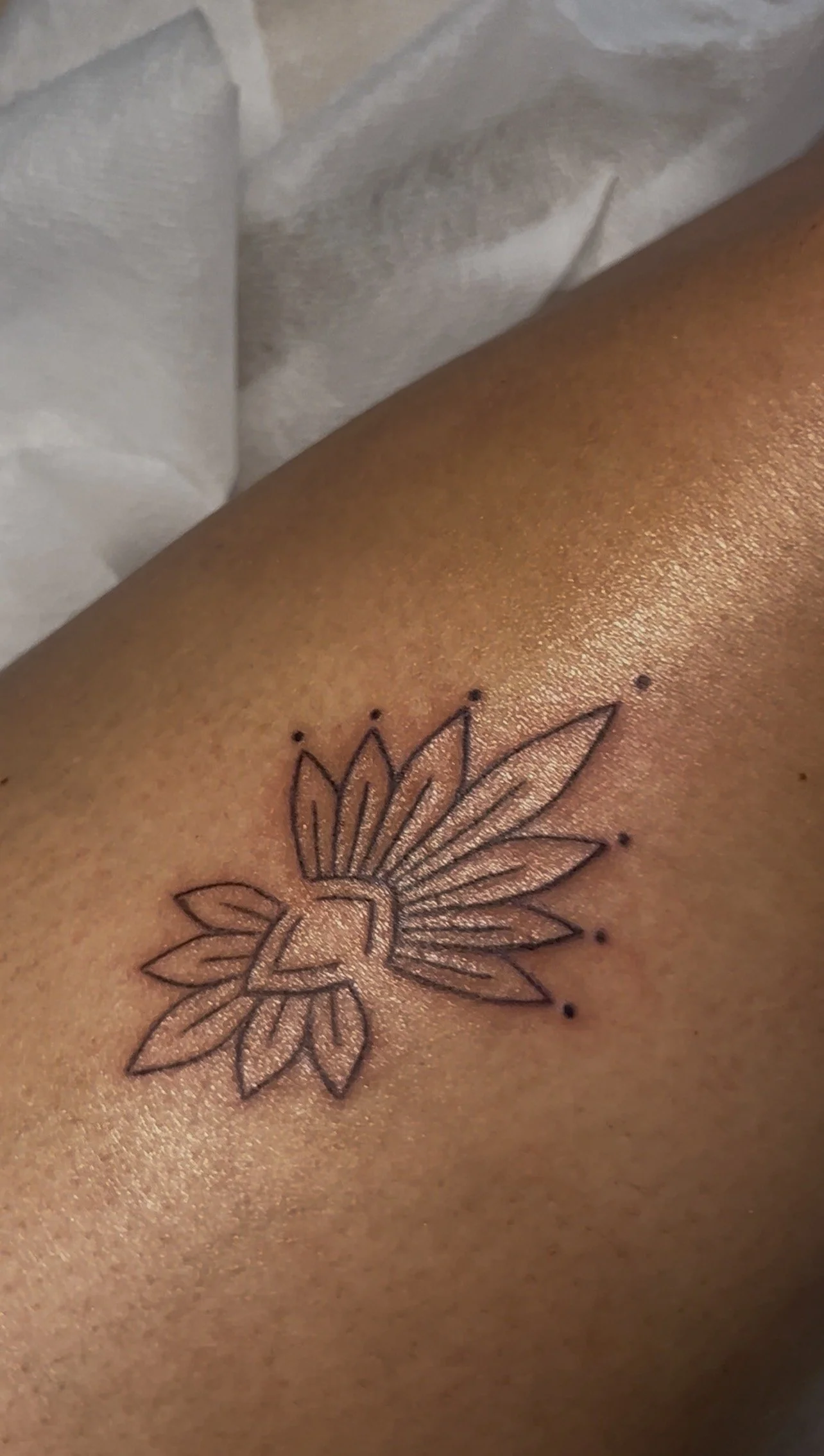 Close-up of a person's skin with a black outline tattoo of a stylized sunflower with pointed petals.