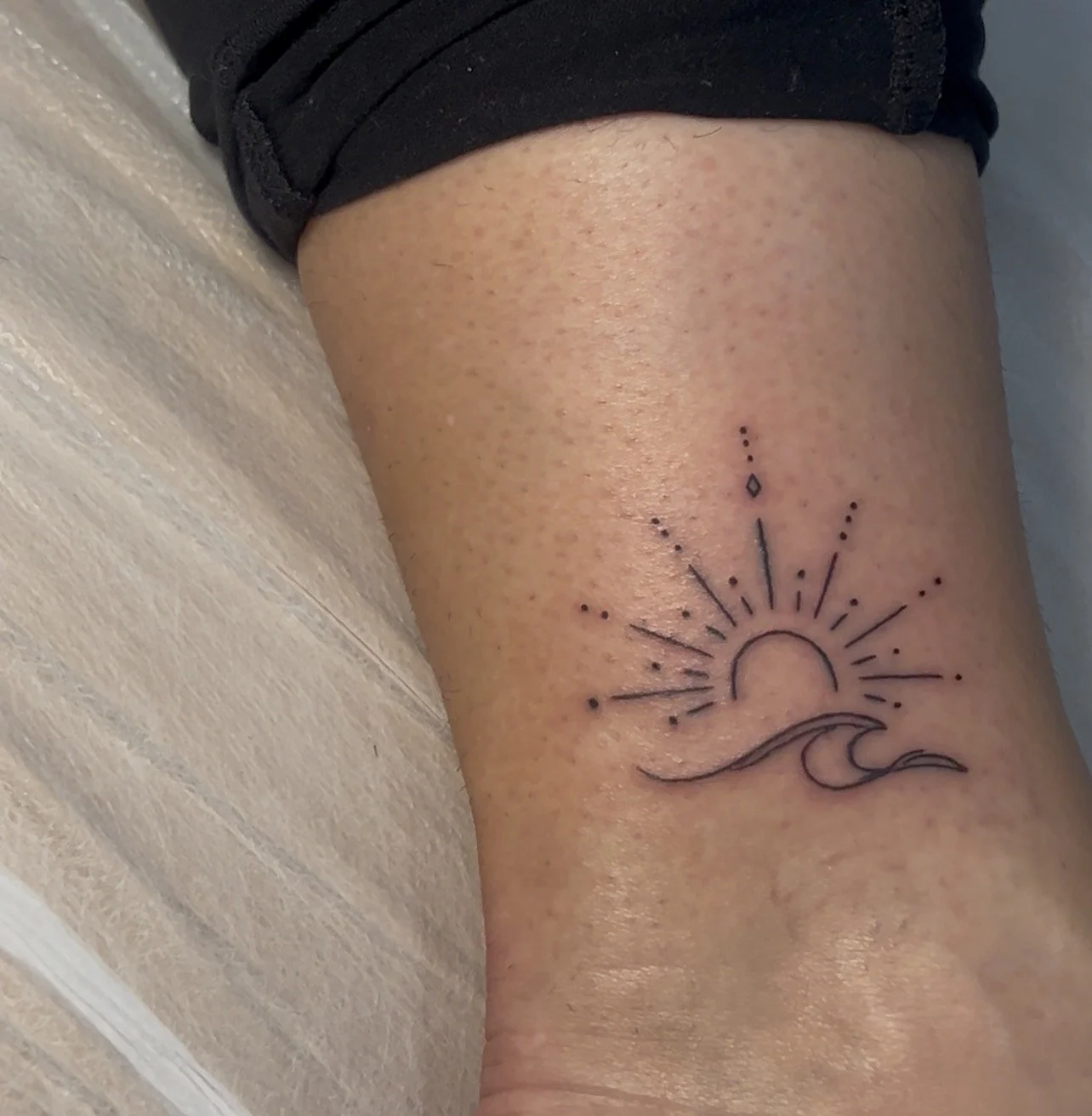 Tattoo of a sunrise over a wave on a person's thigh.