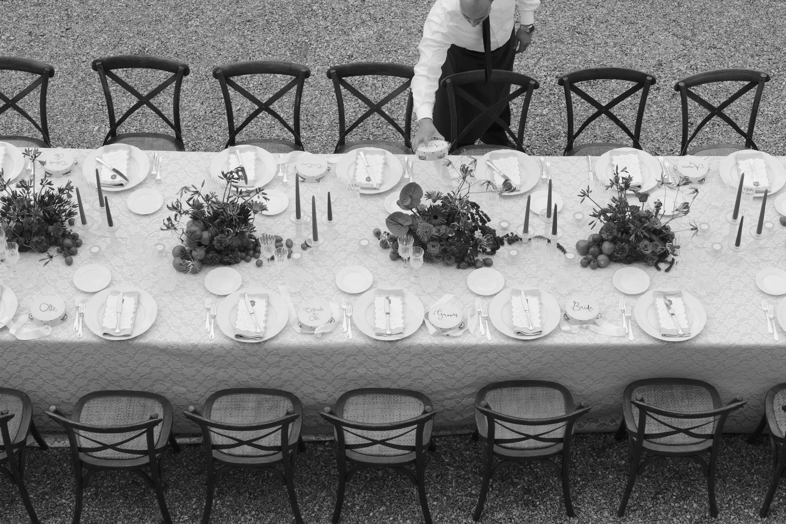 Black-and-white overhead view of the long welcome dinner table with low centrepieces, taper candles and cross-back chairs