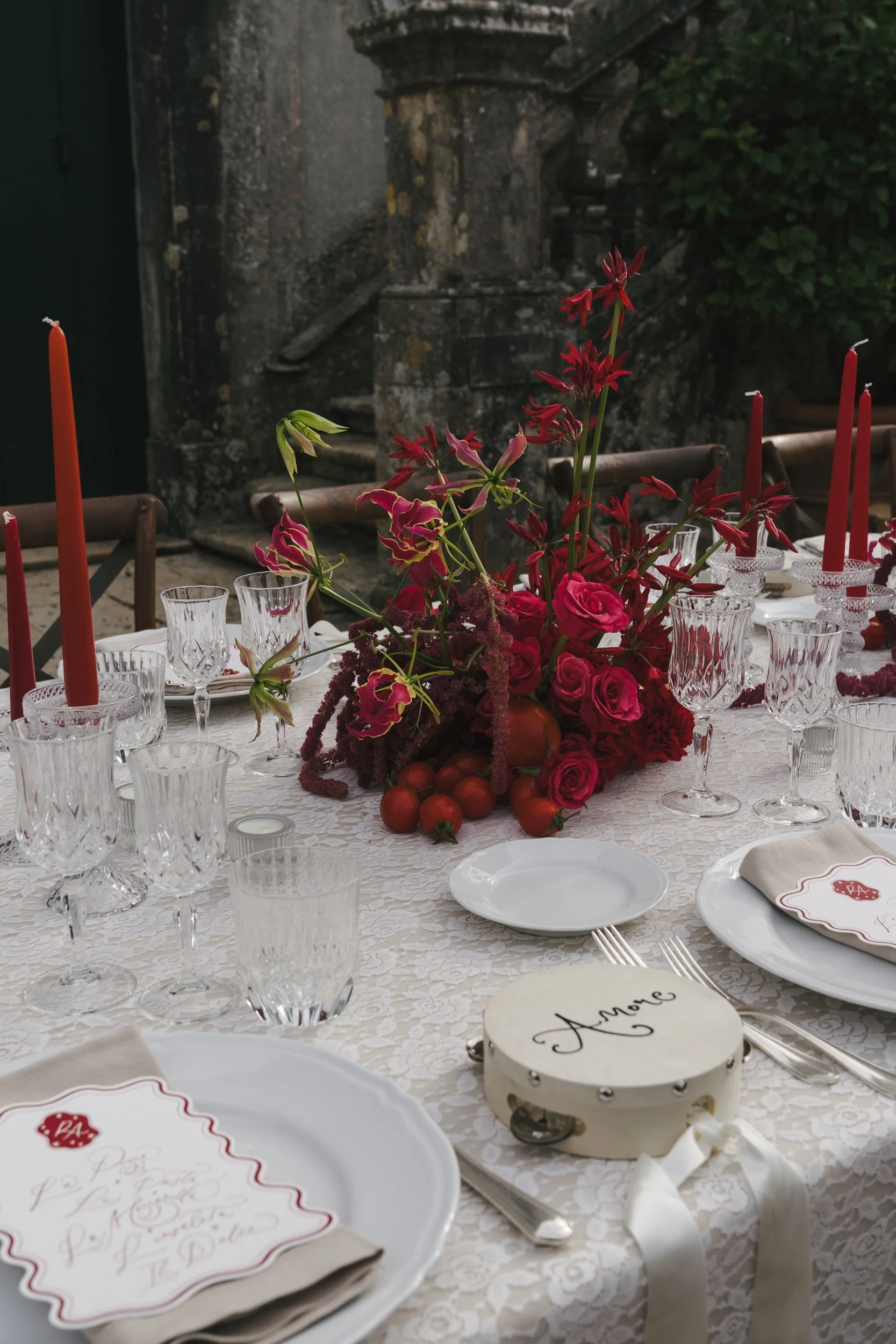 Red rose, gloriosa and dahlia centrepiece with red taper candles above a place setting with calligraphy menu
