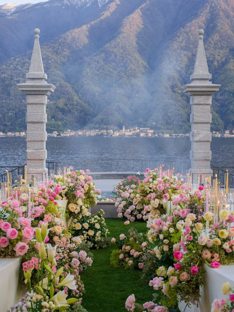 Stone pillars framed by pink and yellow roses and taper candles at dusk on Lake Como