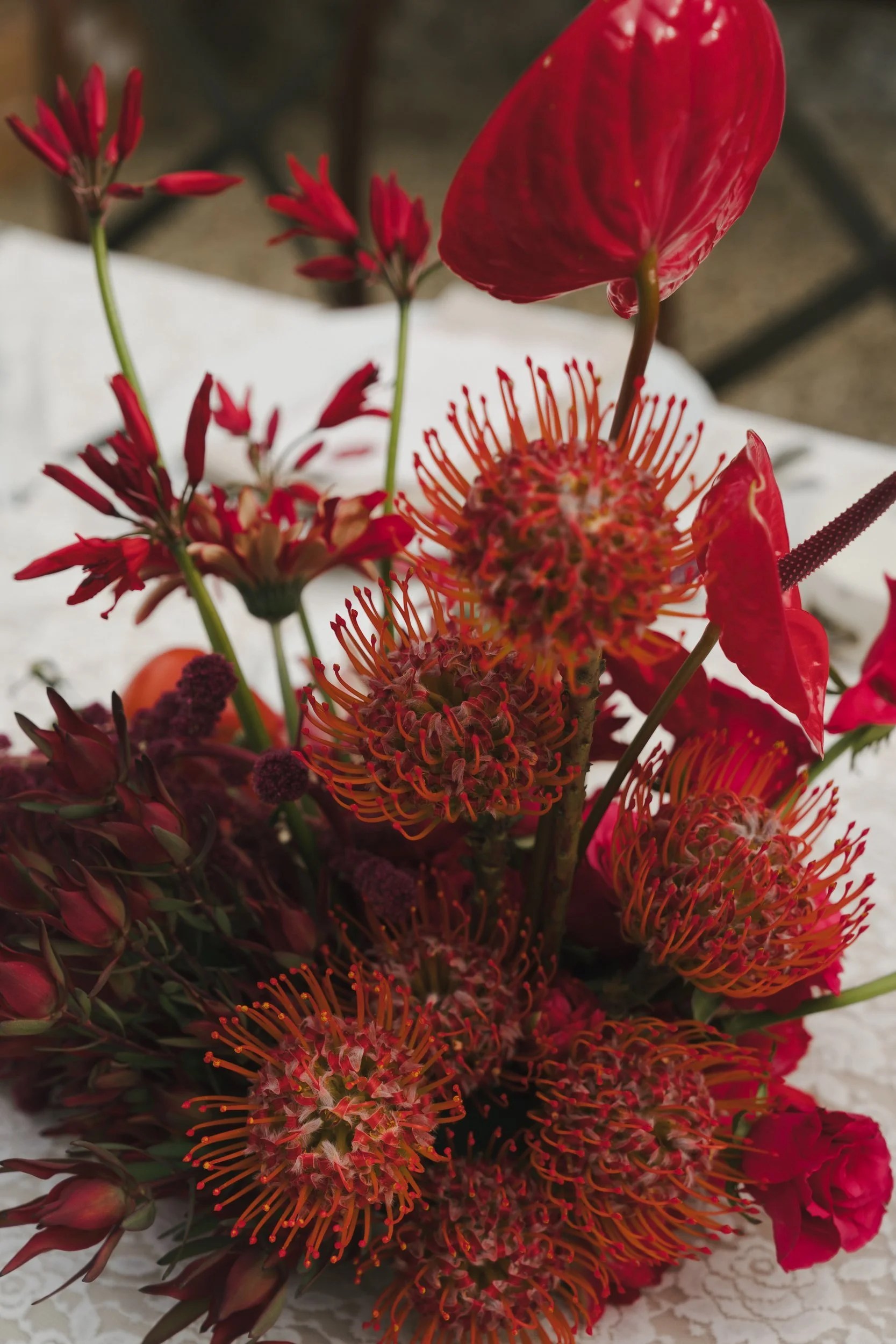 Close-up of red pincushion protea, glossy red anthurium and gloriosa lilies in an autumn wedding arrangement