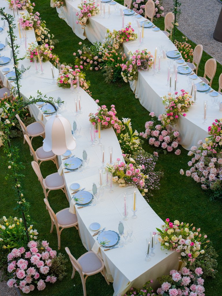 Aerial view of serpentine dinner tables with pastel candles and roses on the lawn