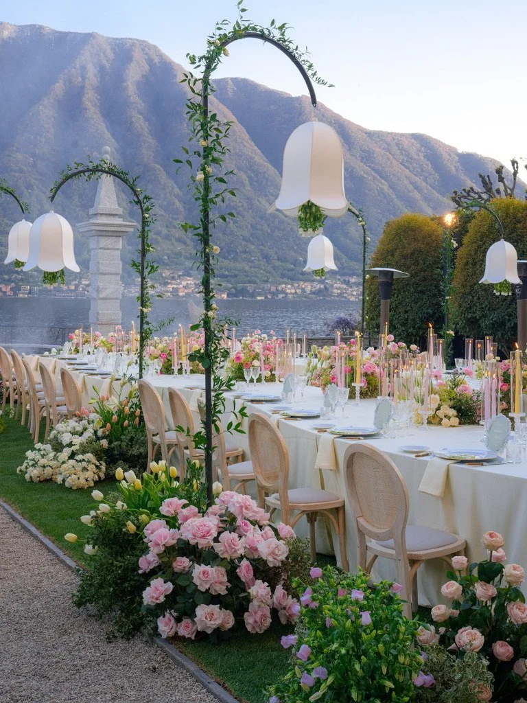 Long dinner table with rattan chairs, pink tapers and garden roses under bell lanterns