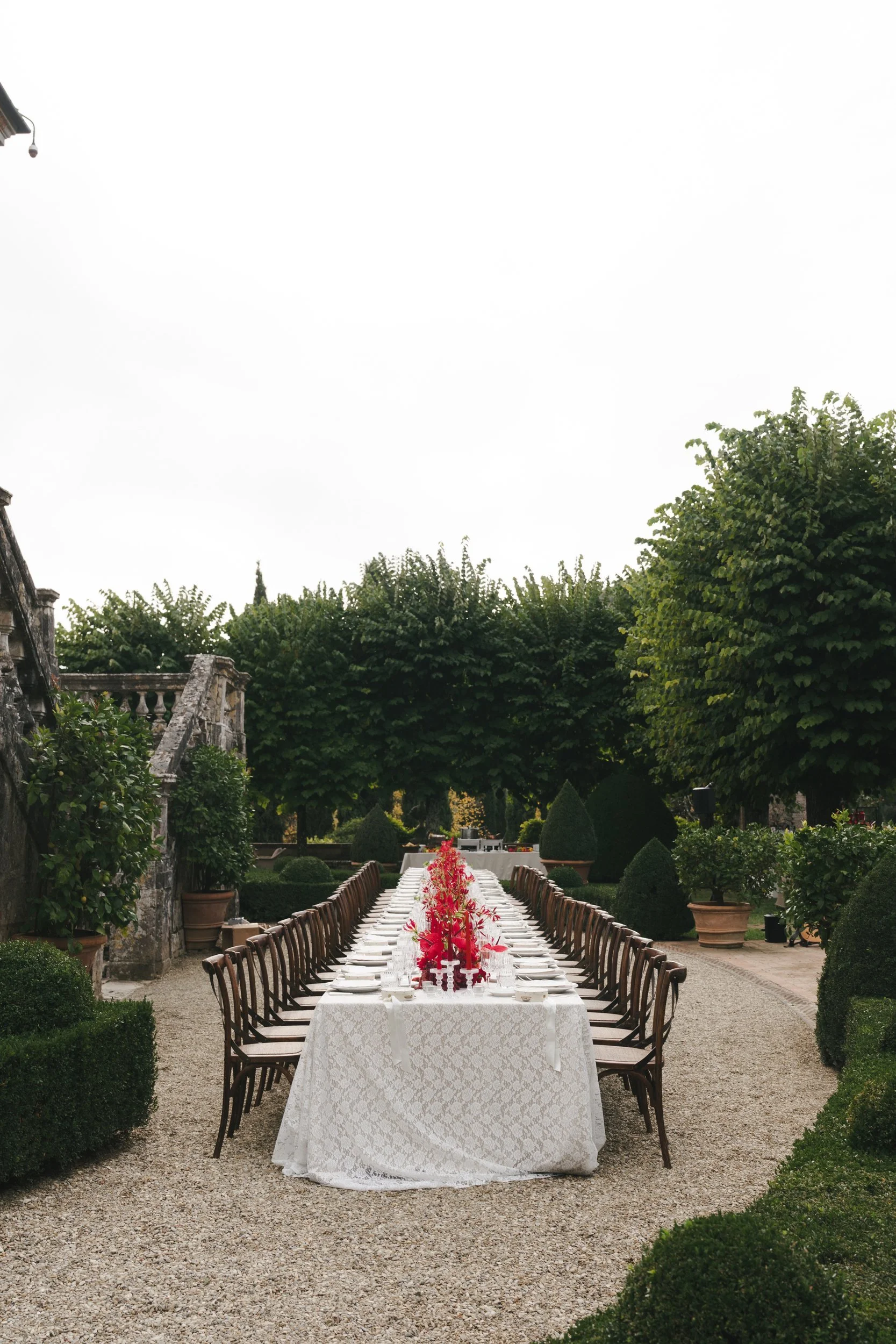 Single long dinner table dressed in vintage lace running through the formal box-hedge gardens of Villa Cetinale