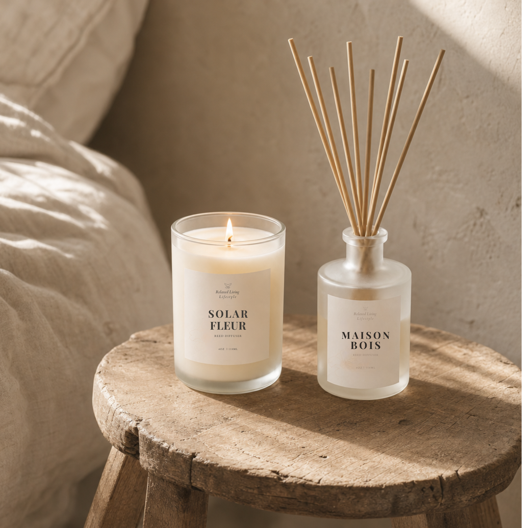 Solar Fleur lit candle and Maison Bois reed diffuser in frosted glass on a rustic wooden stool beside linen bedding