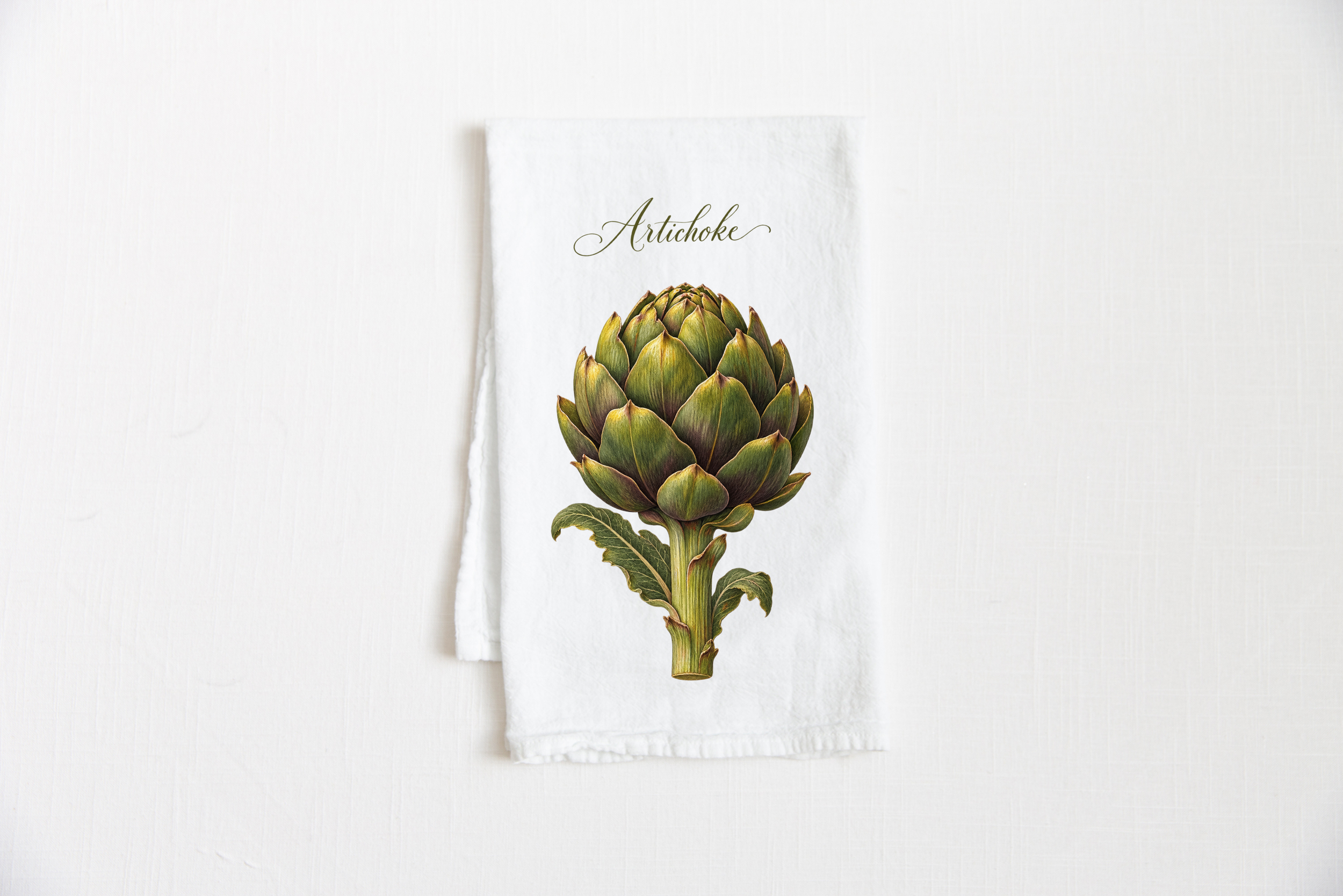 Artichoke Cotton Tea Towel featuring a detailed green and olive botanical artichoke illustration with warm golden accents on a white tea towel