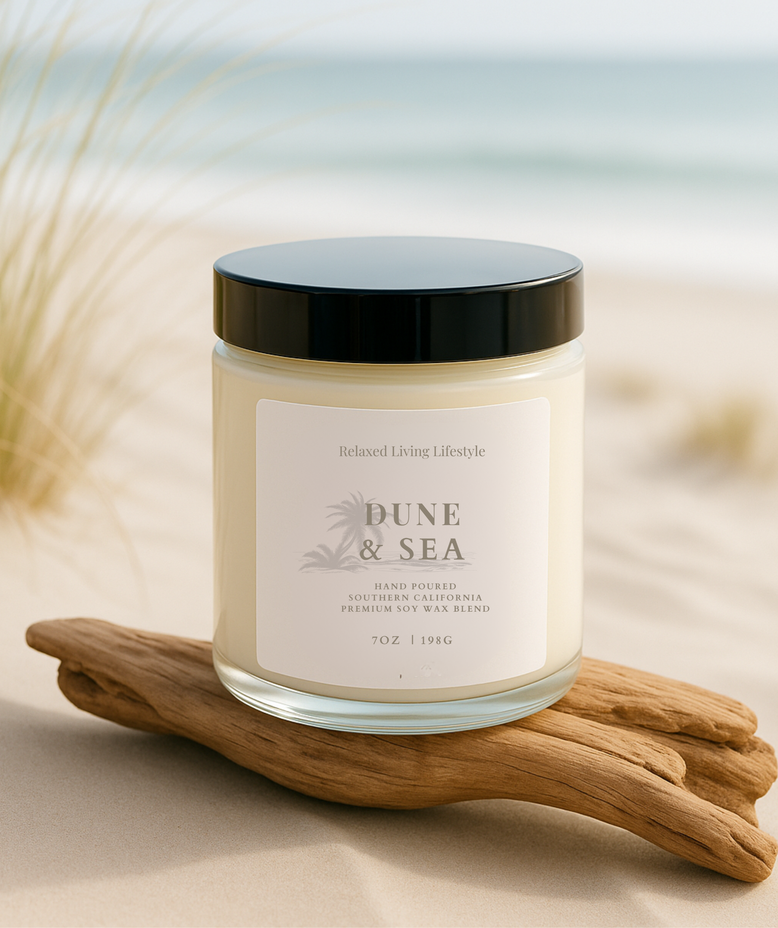 Dune & Sea Candle with lid on, placed on driftwood with ocean and wispy grasses in the background