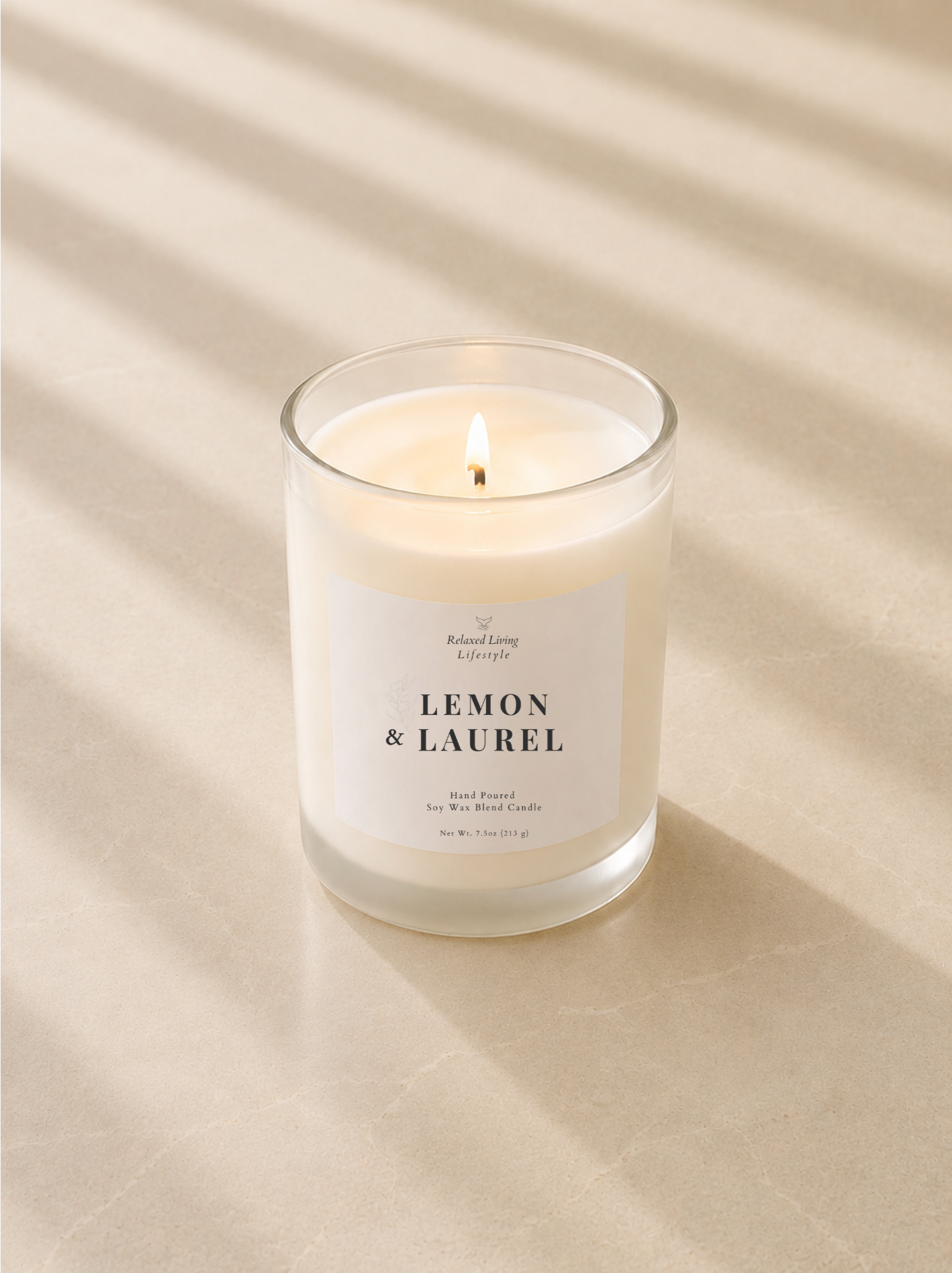 Lit Lemon & Laurel soy wax blend candle in a clear glass vessel on a smooth honed limestone surface with soft afternoon sunlight and elegant diagonal window shadows.