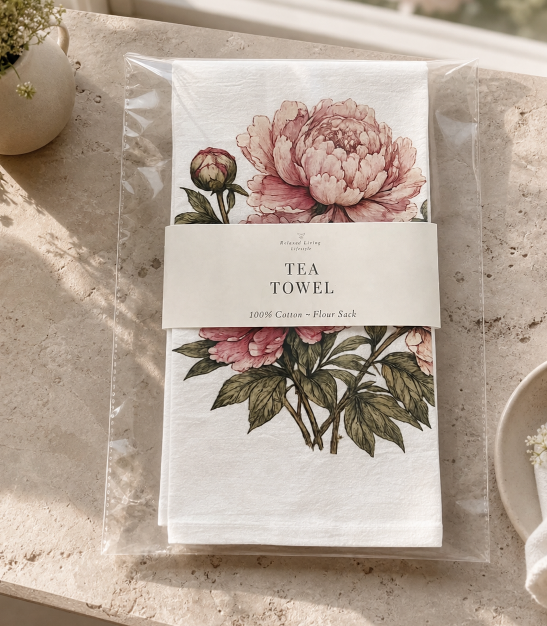 Close-up of packaged Peony cotton tea towel styled in a bright luxury kitchen with branded band featuring elegant floral artwork on soft flour sack cotton kitchen towel