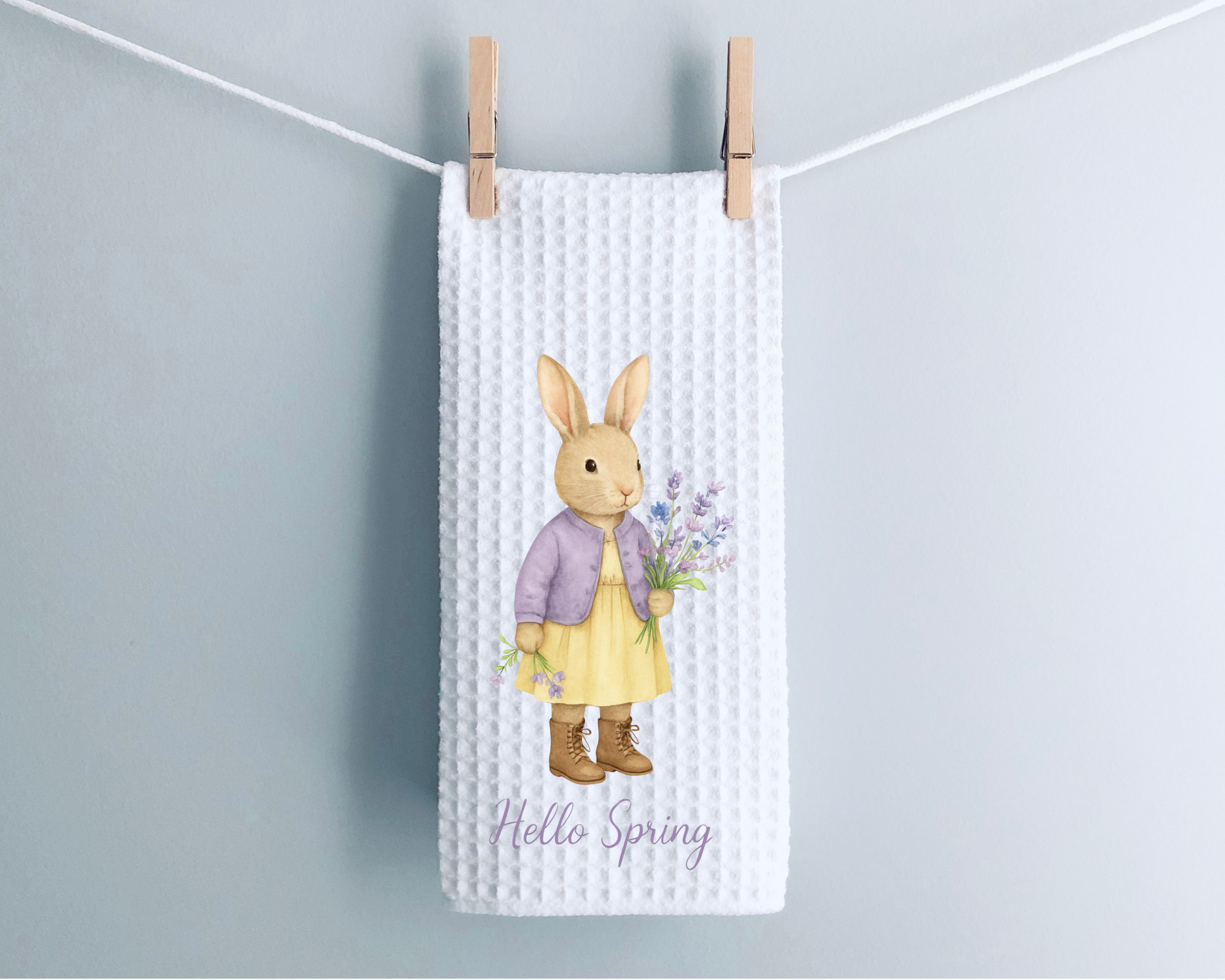 White spring rabbit waffle weave tea towel hanging from clothespins on a neutral background