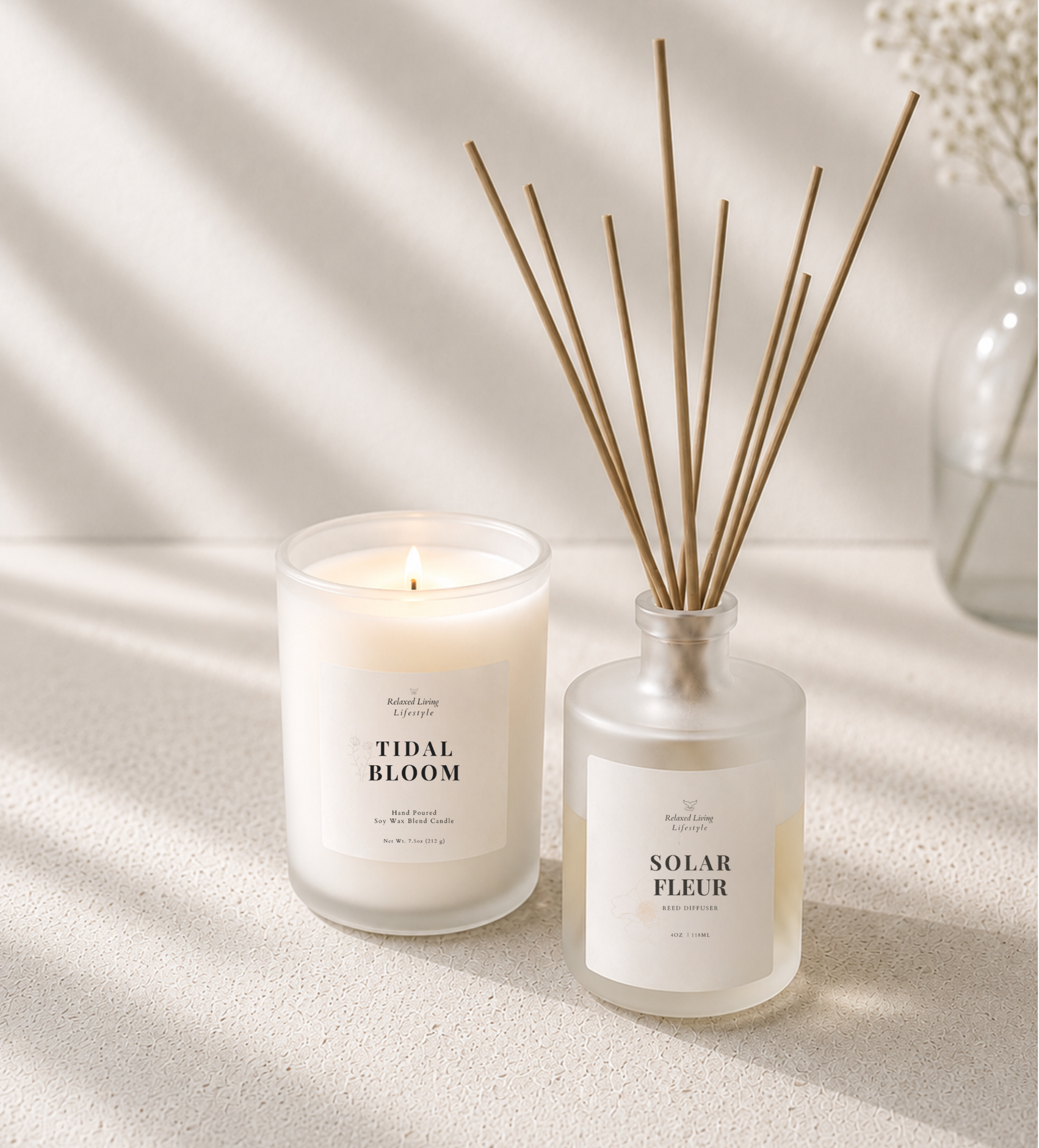 Lit frosted glass soy wax candle and frosted reed diffuser on a light ivory travertine surface with soft afternoon window light and a blurred vase in the background