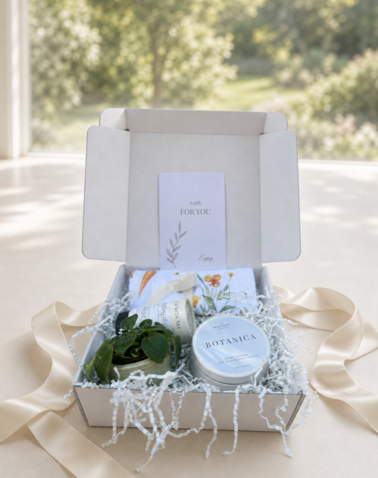 The Garden Gift Set displayed in an open gift box with a BOTANICA candle, floral tea towel, premium tea, and mini potted plant beside satin ribbon.