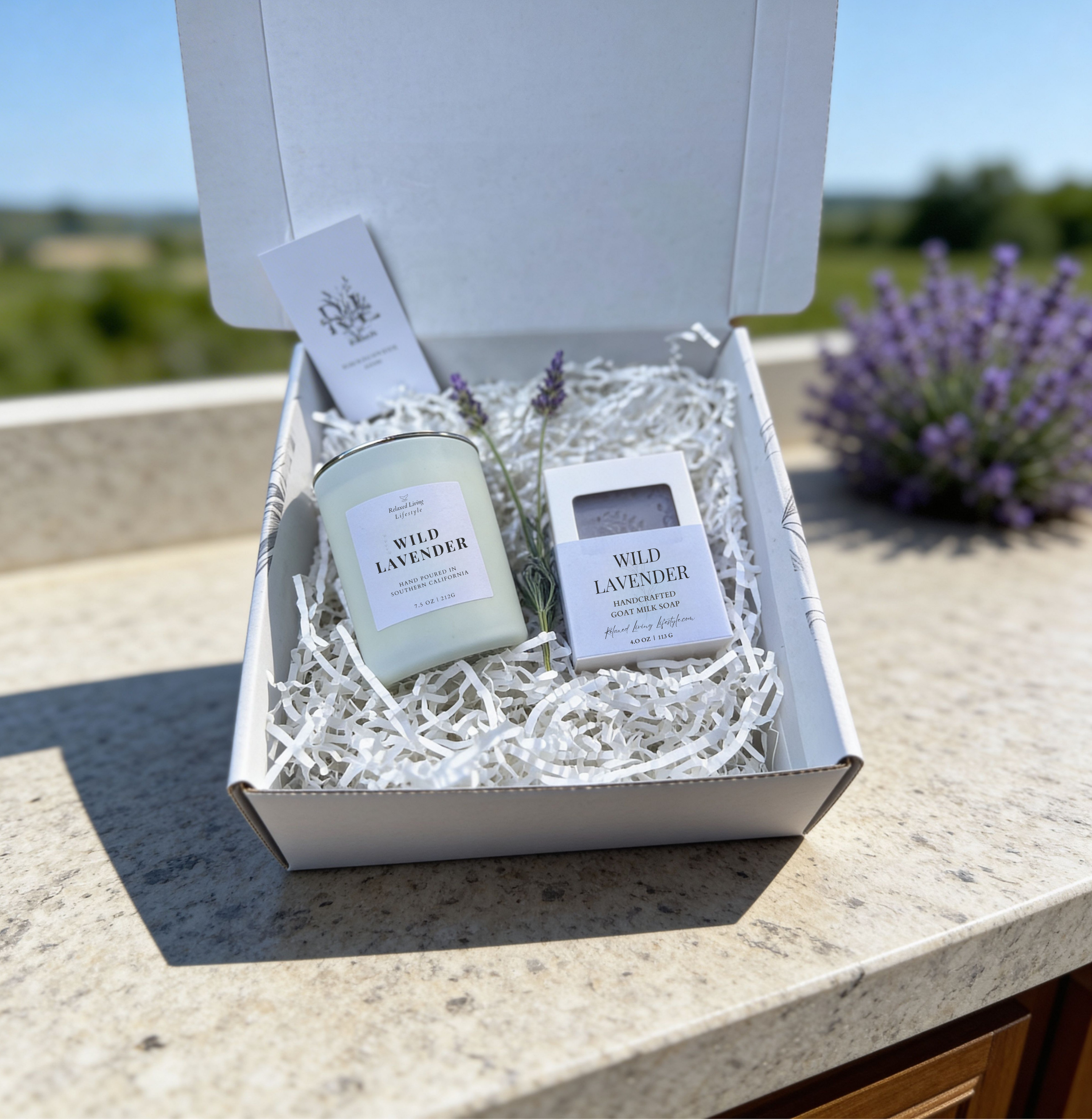 Lavender candle and soap gift set with chamomile, sage, and sandalwood, displayed on a textured surface with blurred greenery and lavender in the background for a calming home fragrance scene