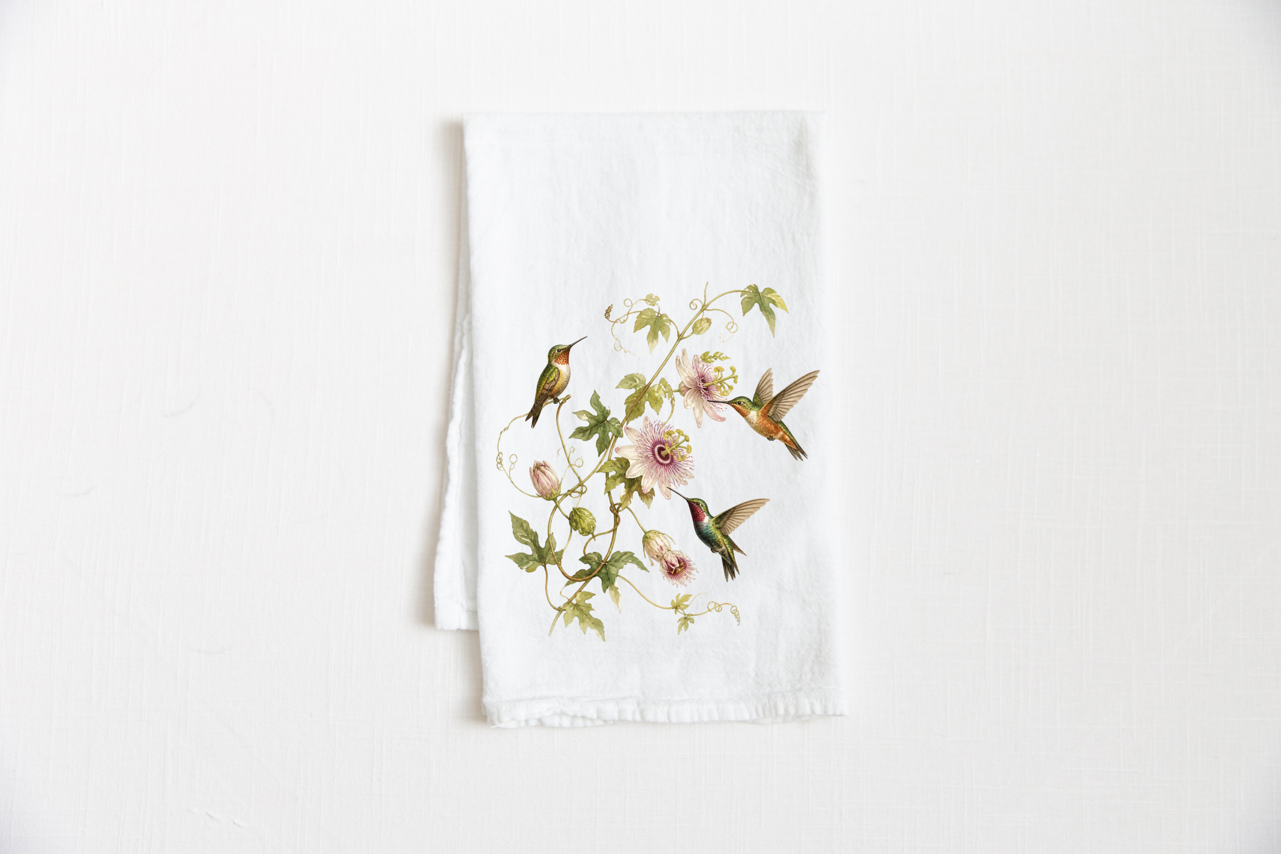 Hummingbird Floral Tea Towel in white cotton featuring three watercolor hummingbirds among pale passionflowers and trailing olive-green vines on white background