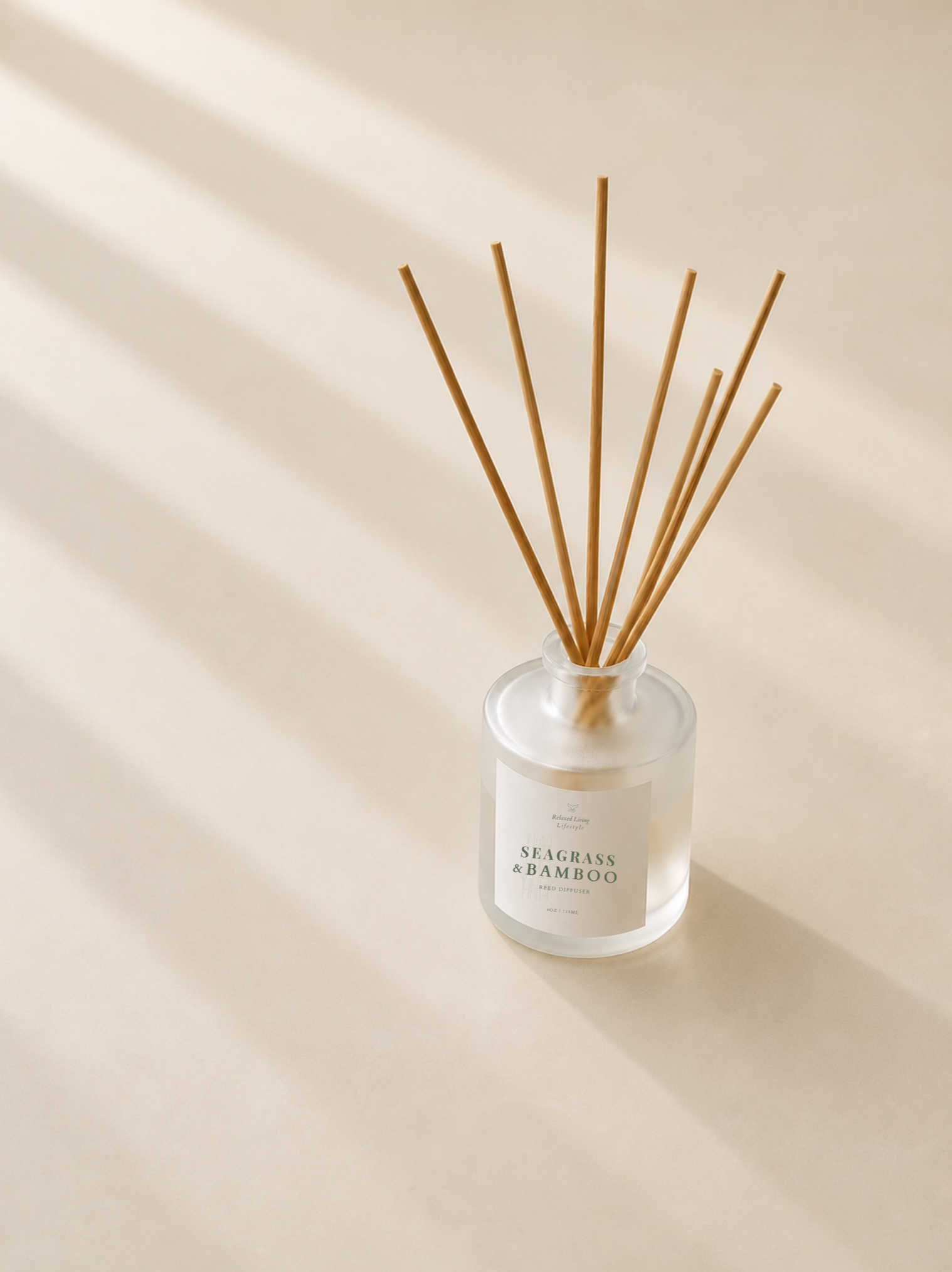 Seagrass & Bamboo reed diffuser in a frosted glass bottle with natural reeds on a smooth honed limestone surface, illuminated by soft afternoon sunlight casting elegant diagonal window shadows.