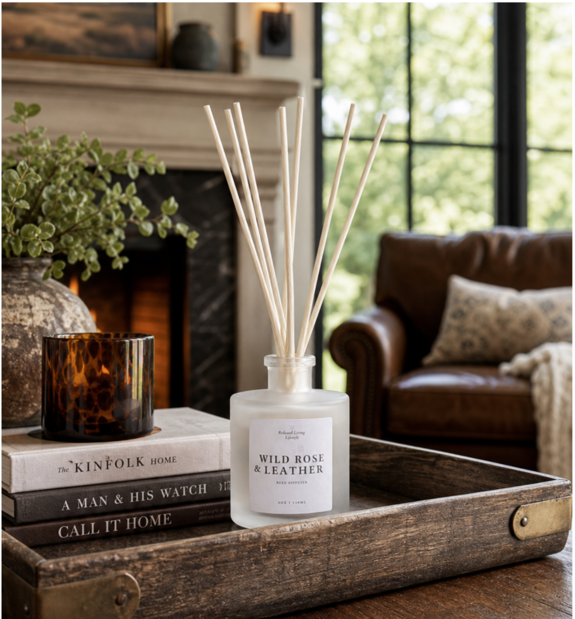 “Wild Rose & Leather reed diffuser styled on a rustic wood tray in a modern rustic living room with fireplace, neutral decor, and greenery views.”