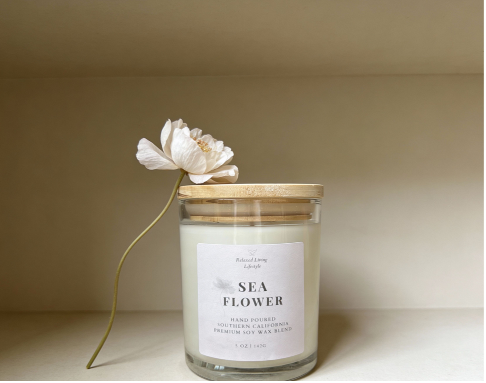 Sea Flower 5 oz soy candle on shelf with flower accent. Hand-poured coastal floral candle with lid with notes of jasmine, honeydew, sandalwood, and marine notes.