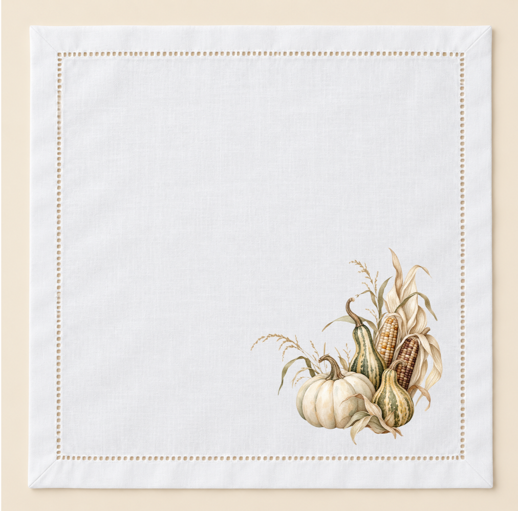 White 20-inch hemstitched cotton napkin with a coordinating hand-pressed harvest design featuring autumn botanicals in soft wheat, olive, cream, and brown tones.